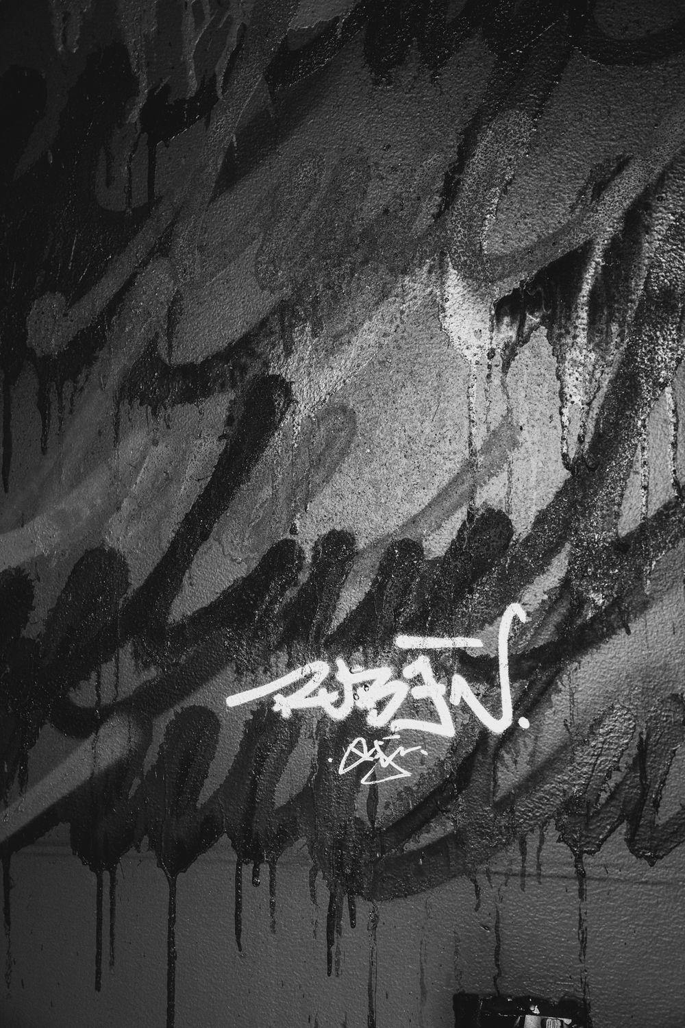 Black and white graffiti art on a wall featuring bold brushstrokes and white tag signature reading Ruben.
