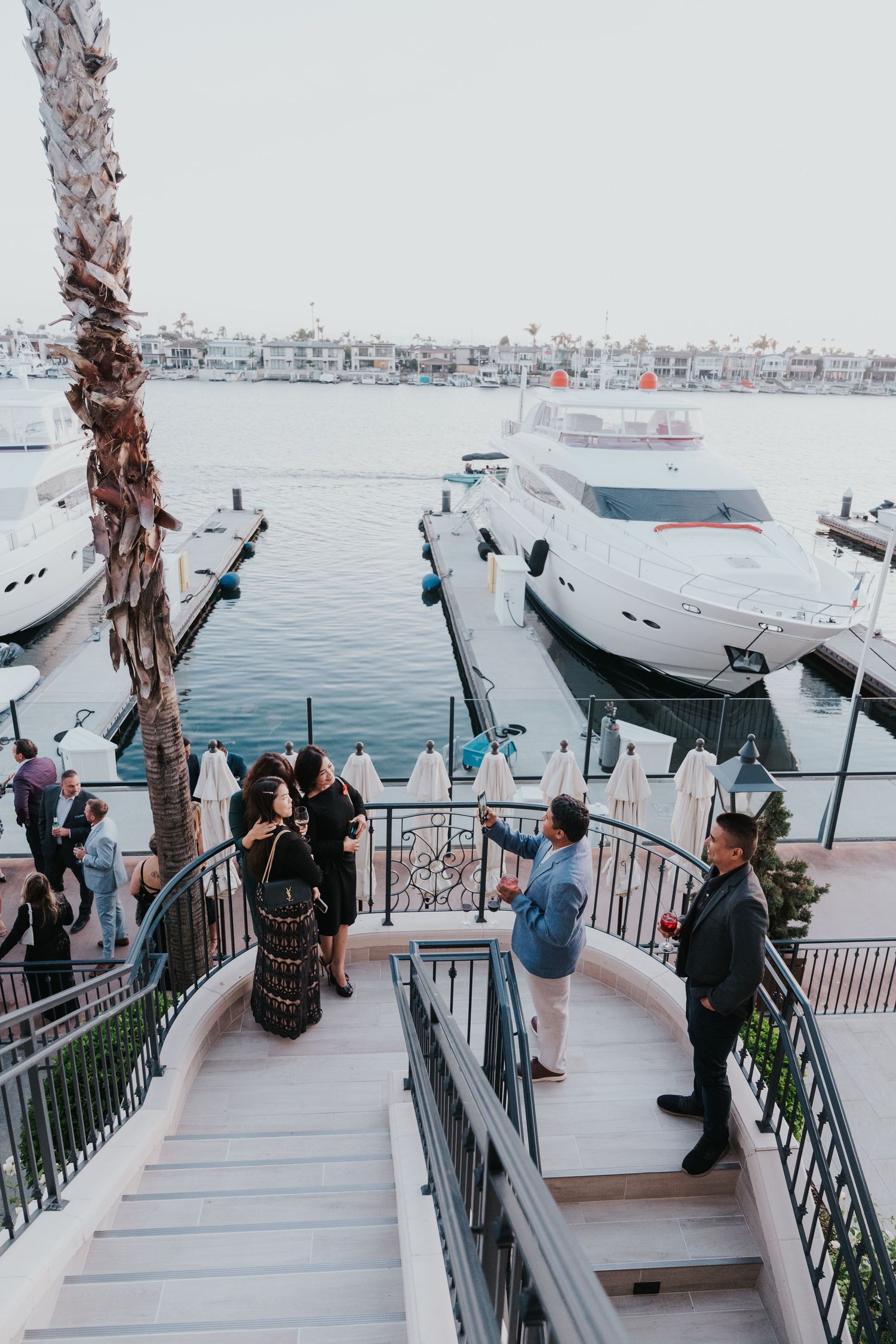 Guests gather on elegant marina stairs beside luxury yachts docked at a waterfront venue during an evening event.
