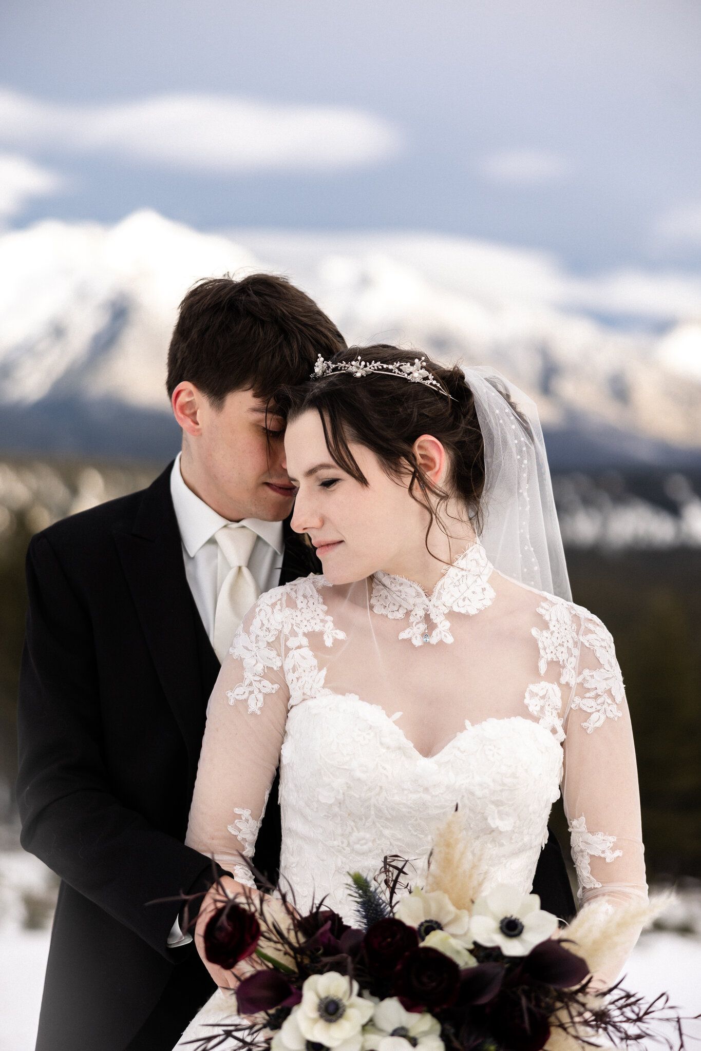 Groom embracing the bride with her anemone bouquet, snowy Rocky Mountain peaks behind them in Banff