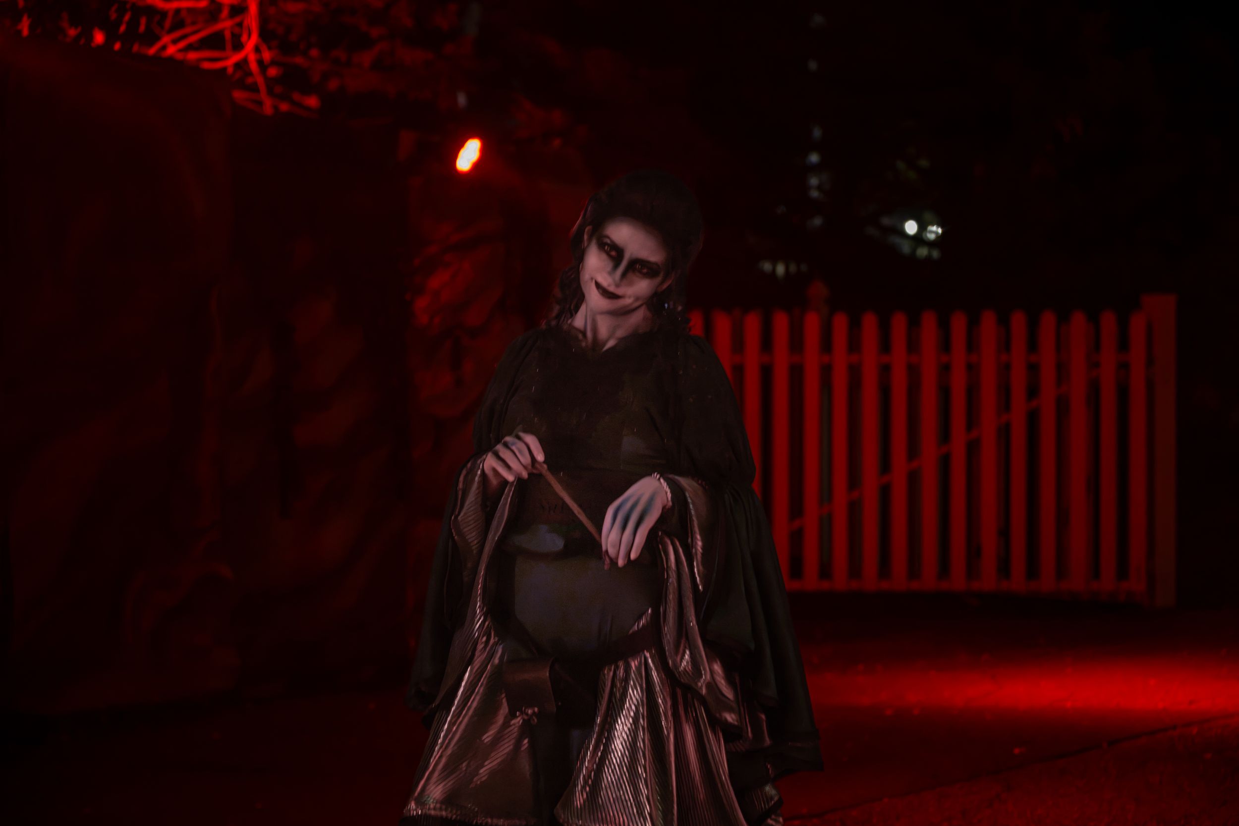 Person in dramatic Halloween costume with skull makeup and dark cape posed under red lighting outdoors.