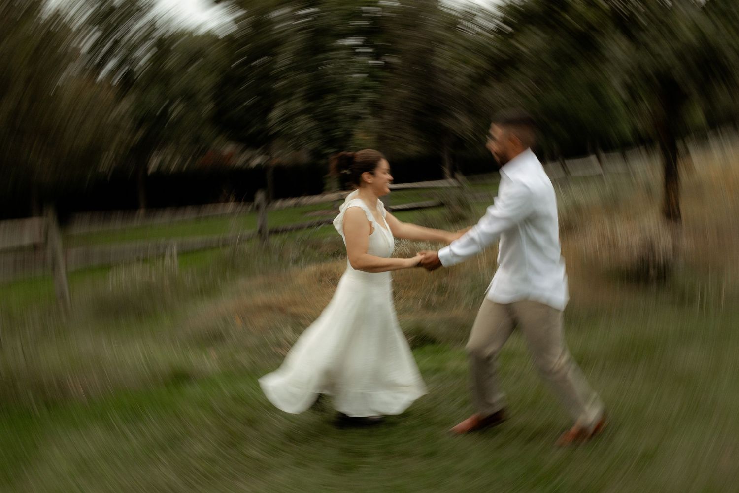 A bride and groom joyfully spin together in a field, captured with a dreamy motion blur effect.