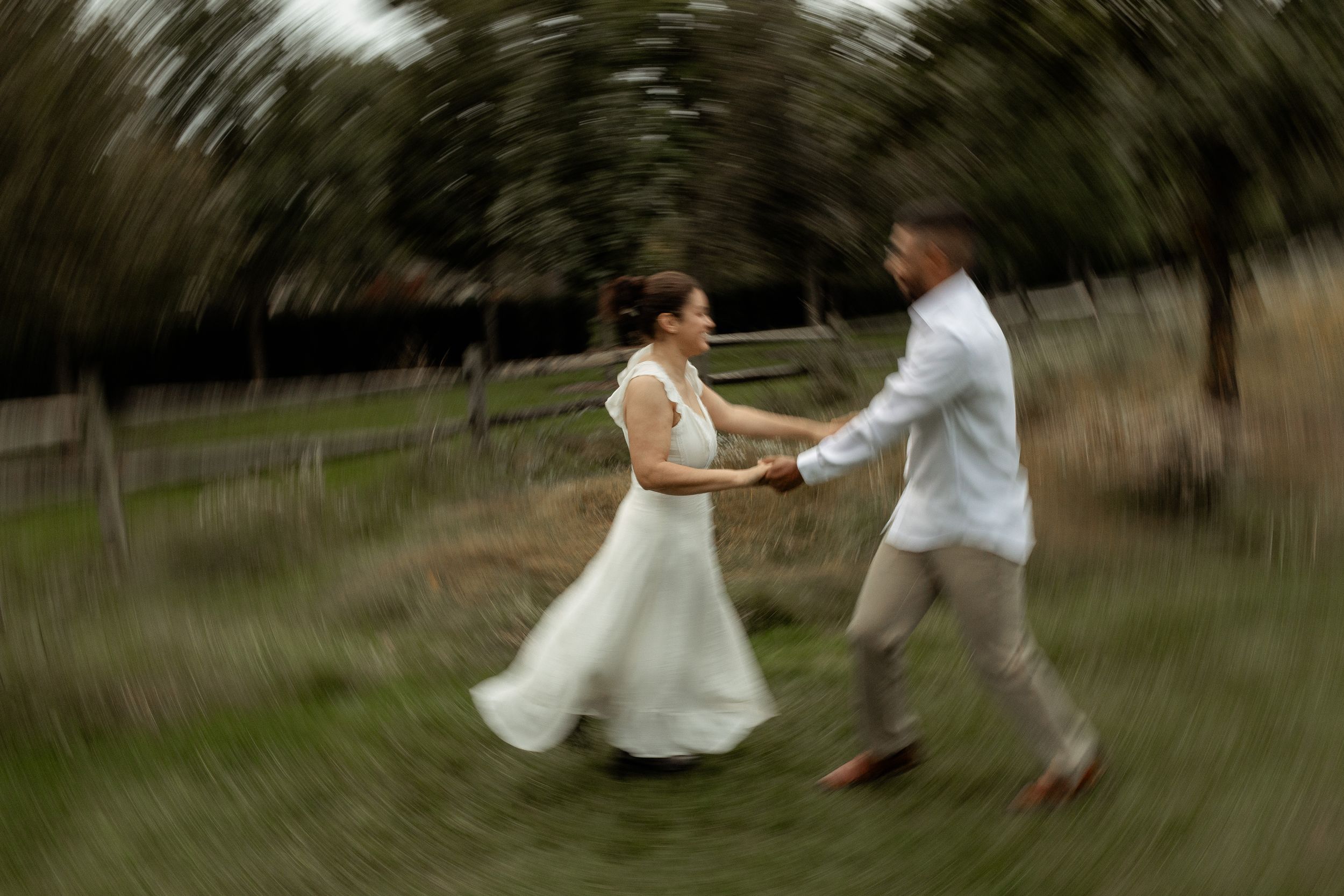 A bride and groom joyfully spin together in a field, captured with a dreamy motion blur effect.