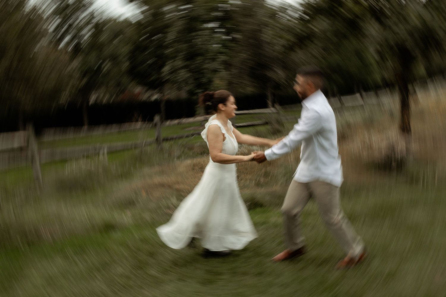 A bride and groom joyfully spin together in a field, captured with a dreamy motion blur effect.
