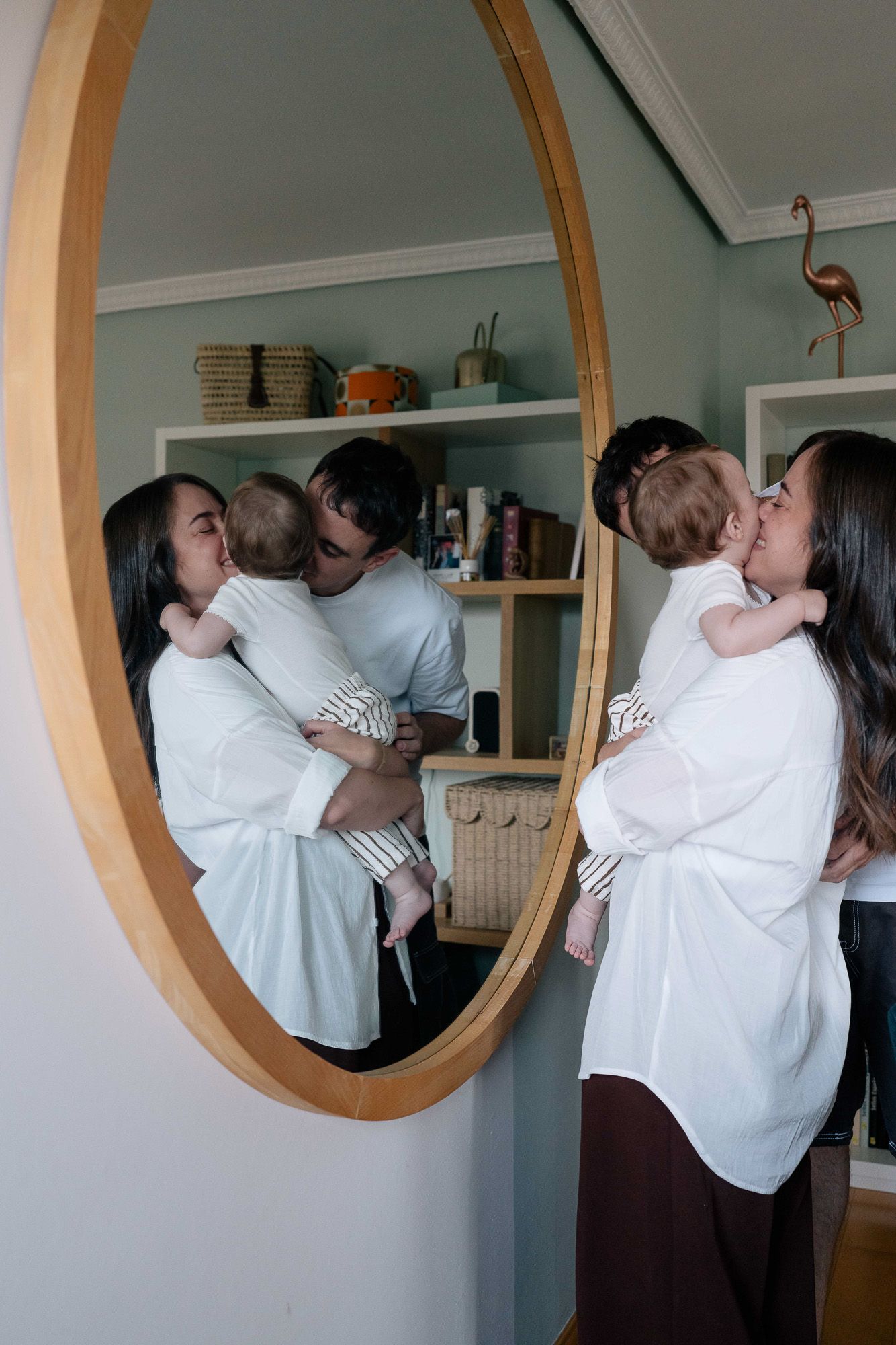 A young family shares a tender mealtime moment, with a baby in a high chair being fed by loving parents at home.