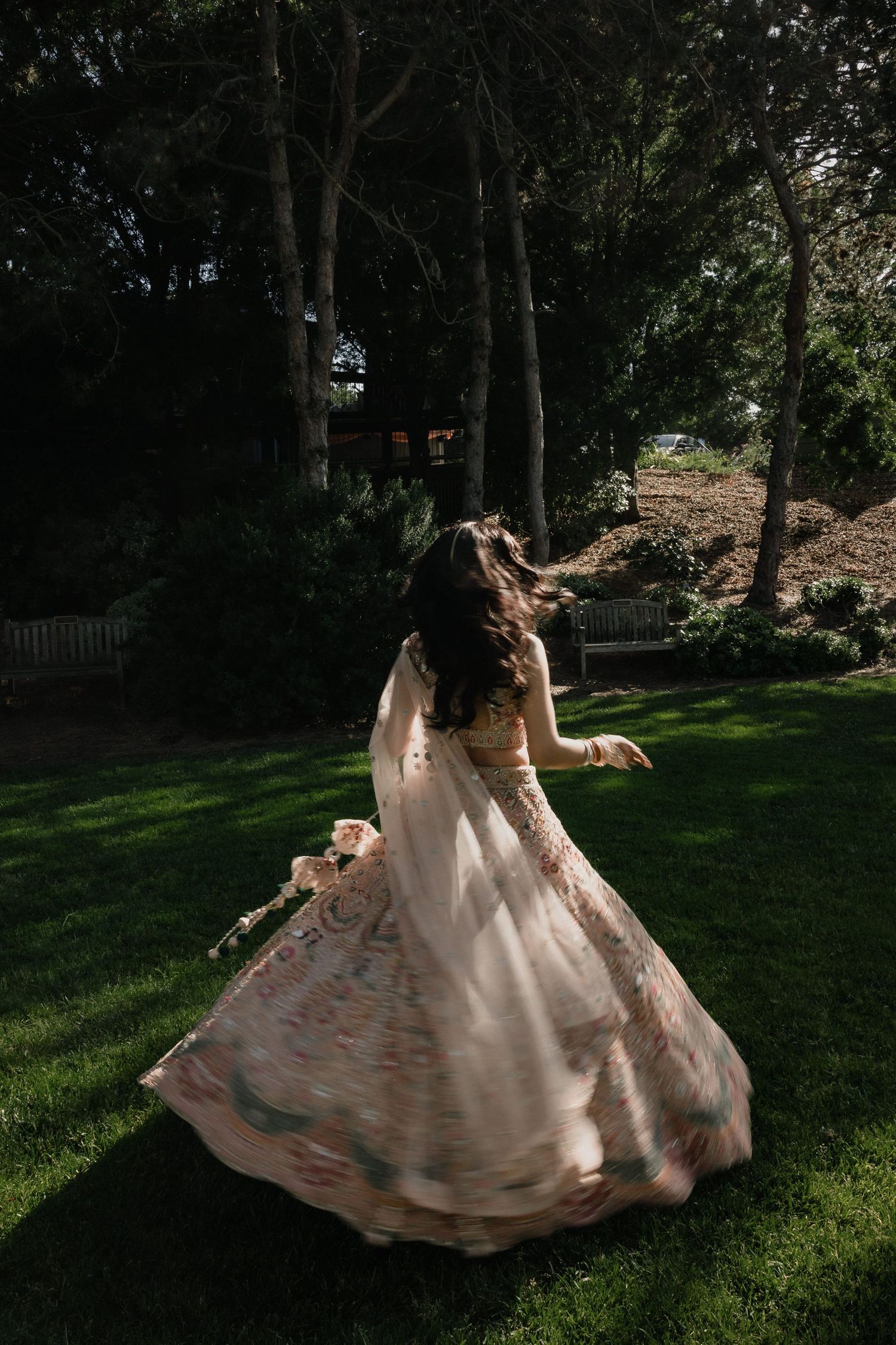 Bride twirling in a blush pink floral embroidered lehenga in a lush green garden during her wedding day.