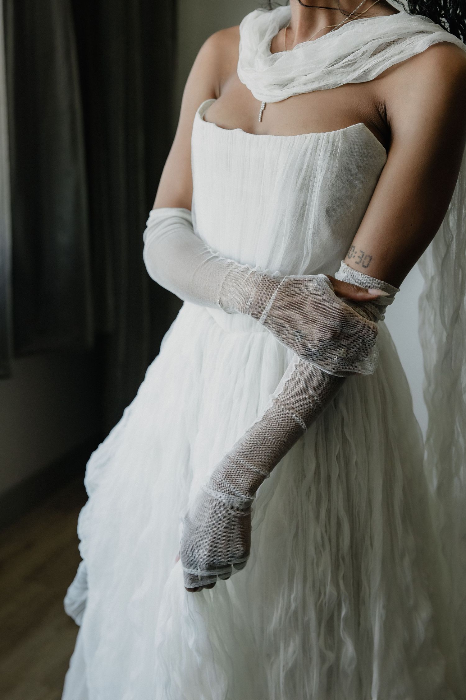 Bride wearing white tulle strapless wedding dress with sheer elbow-length gloves and draped scarf.