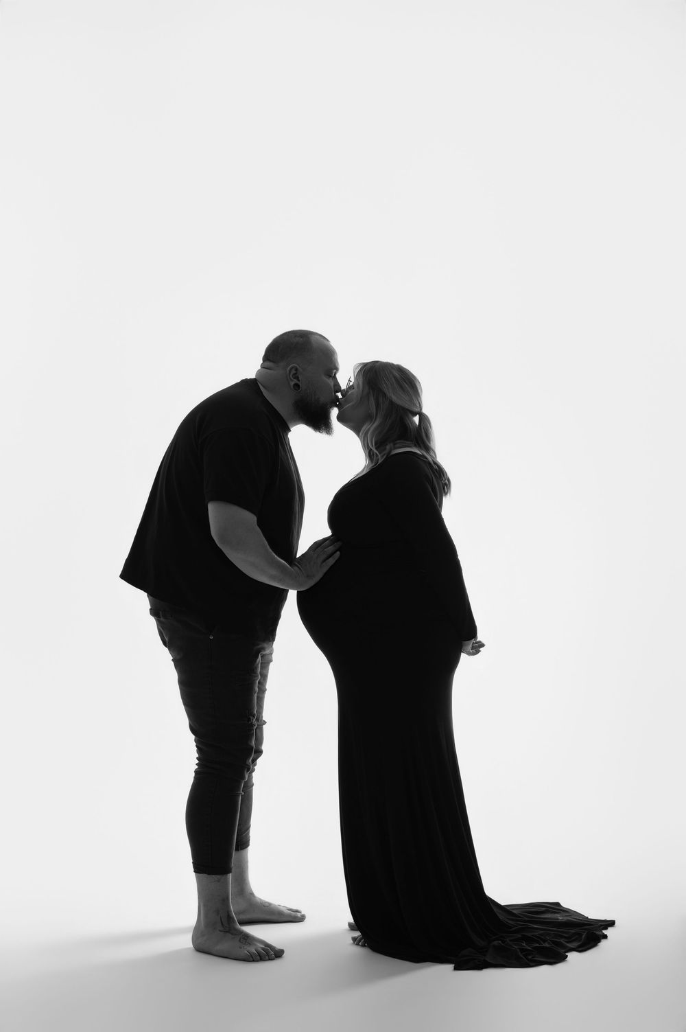 Pregnant woman with red hair poses in a flowing beige chiffon maternity gown against a neutral studio backdrop.