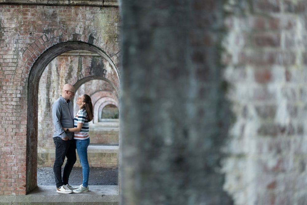 Couple standing romantically under brick archways in a historic outdoor setting.