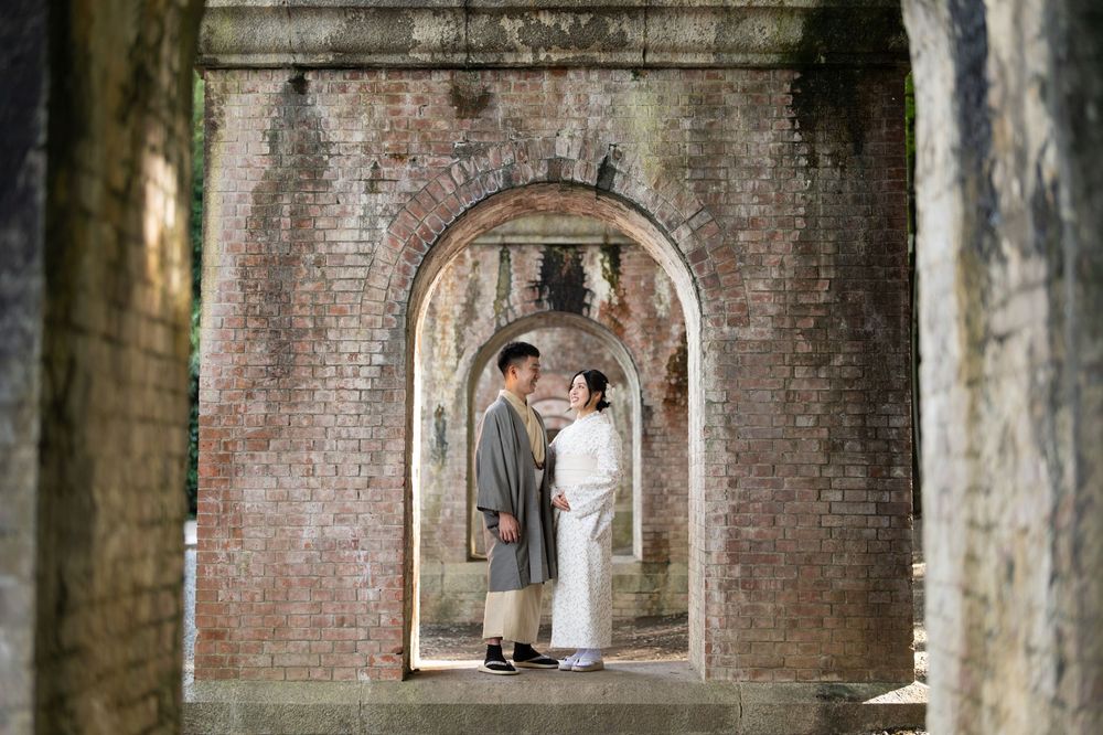 Couple in traditional attire standing under brick archways at a historic site.