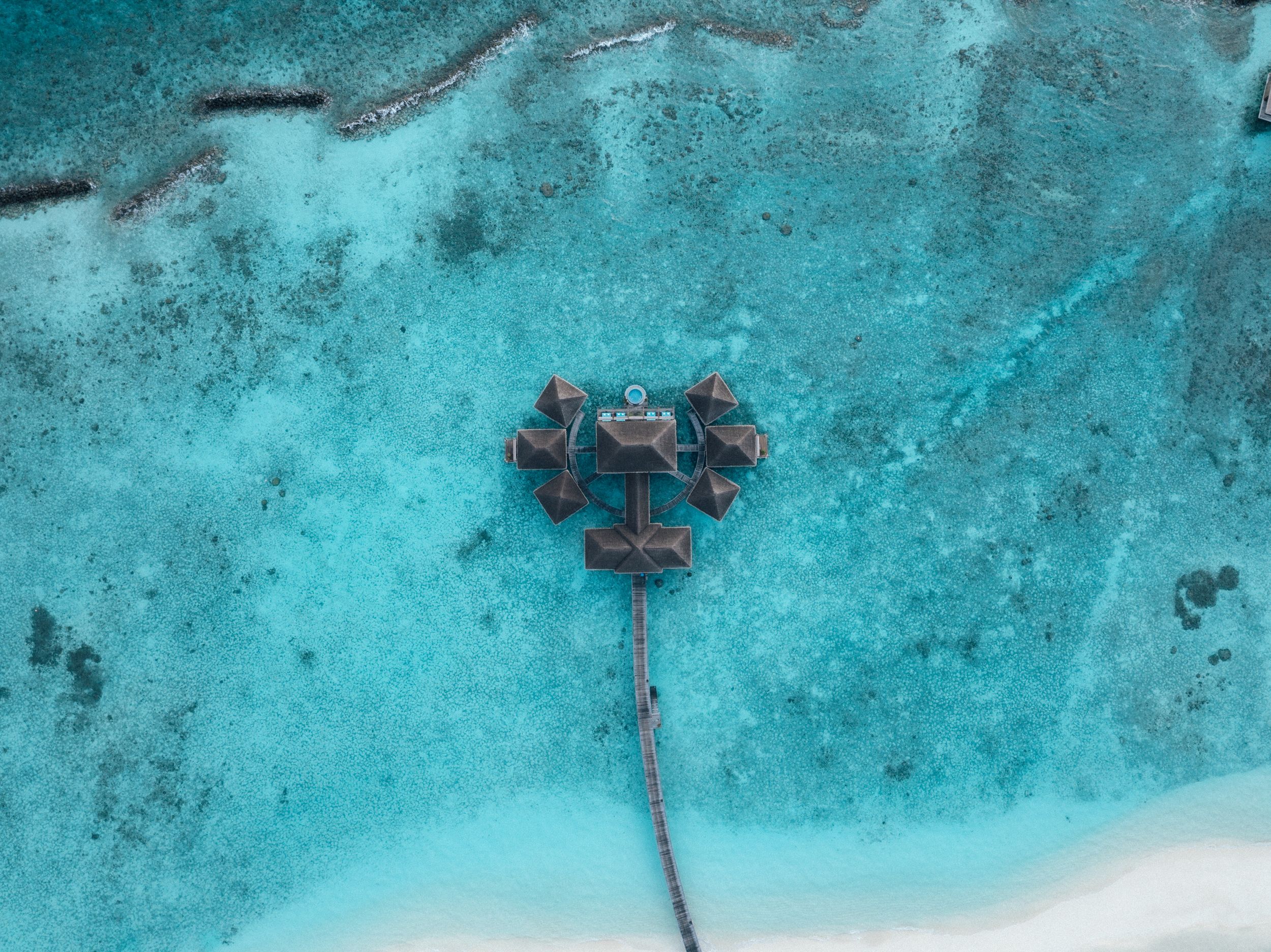 Aerial view of overwater bungalows connected by a dock in stunning turquoise Maldives waters.