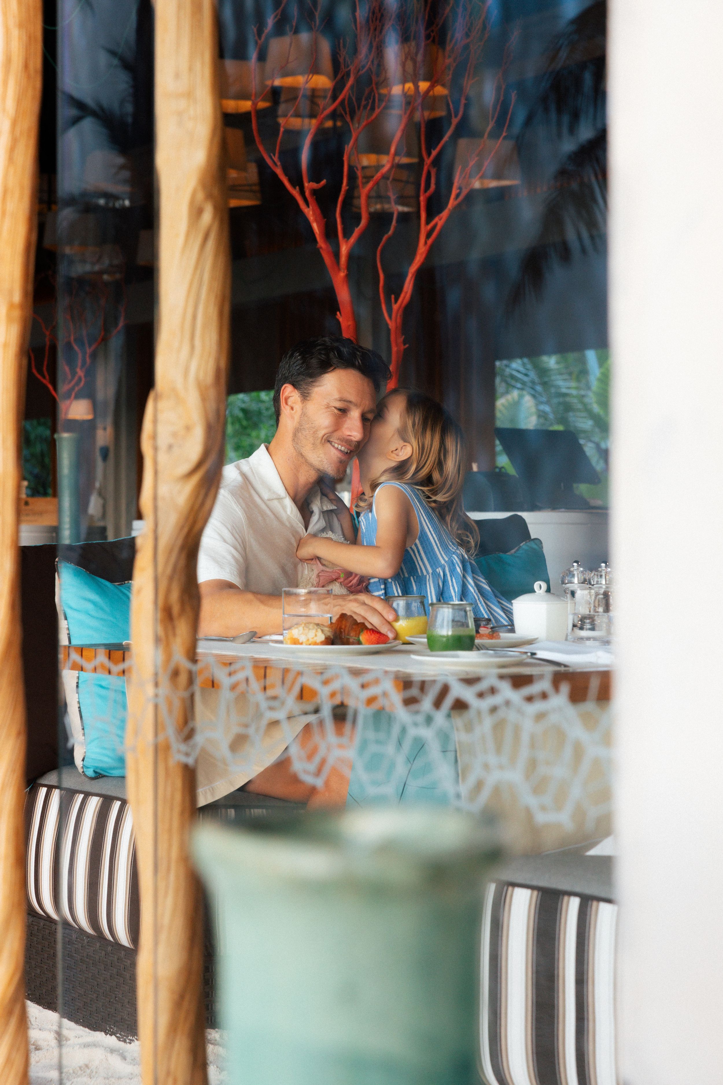 A couple shares a romantic moment while dining at an elegant restaurant, viewed through a glass window.