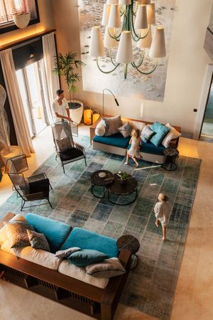 An overhead view of a luxurious living room with teal sofas, a family, and a decorative chandelier.