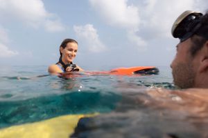 Two surfers floating on colorful boards in calm ocean water, smiling at each other on a sunny day.