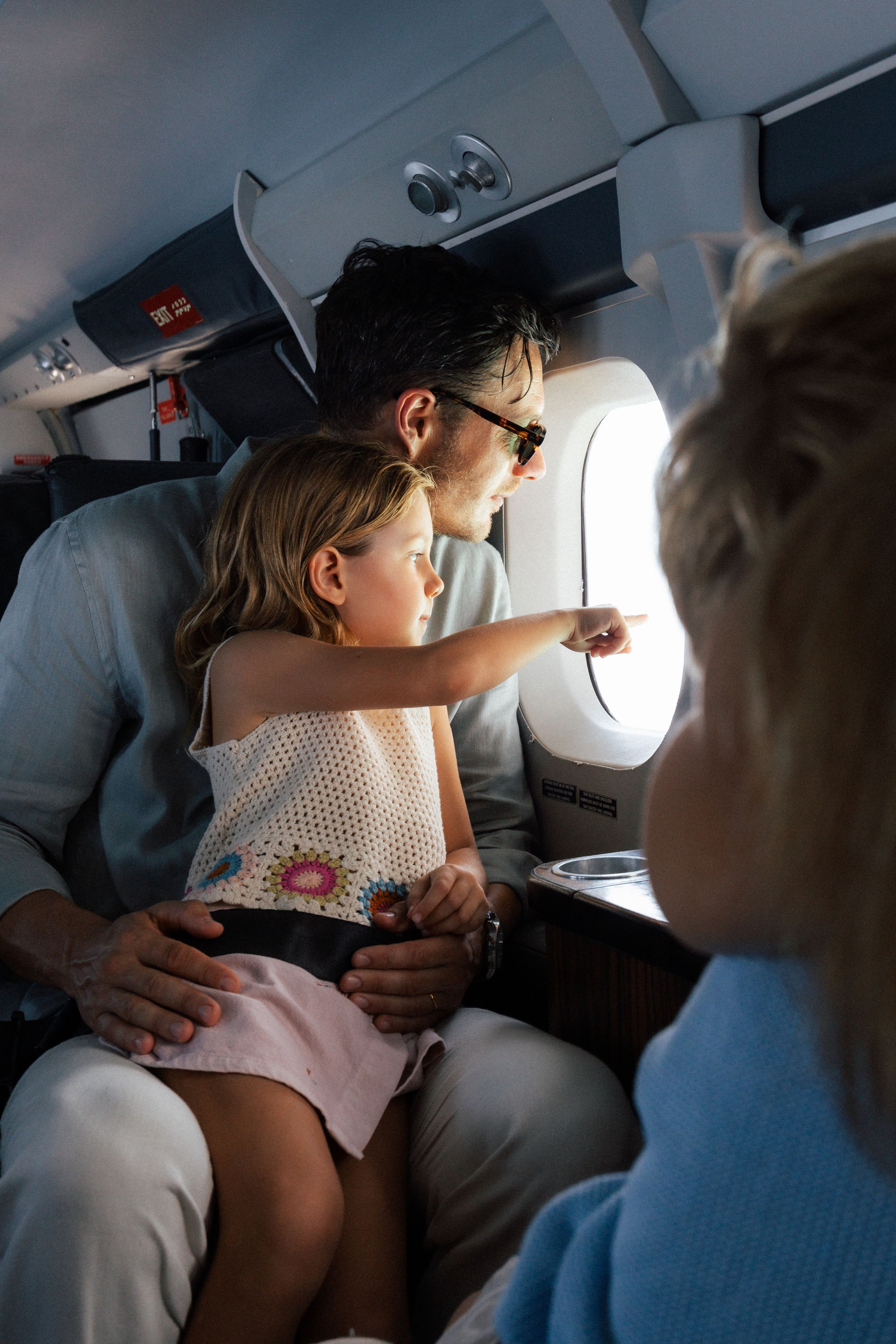 A father and daughter look out the window of a private jet during a family flight vacation.