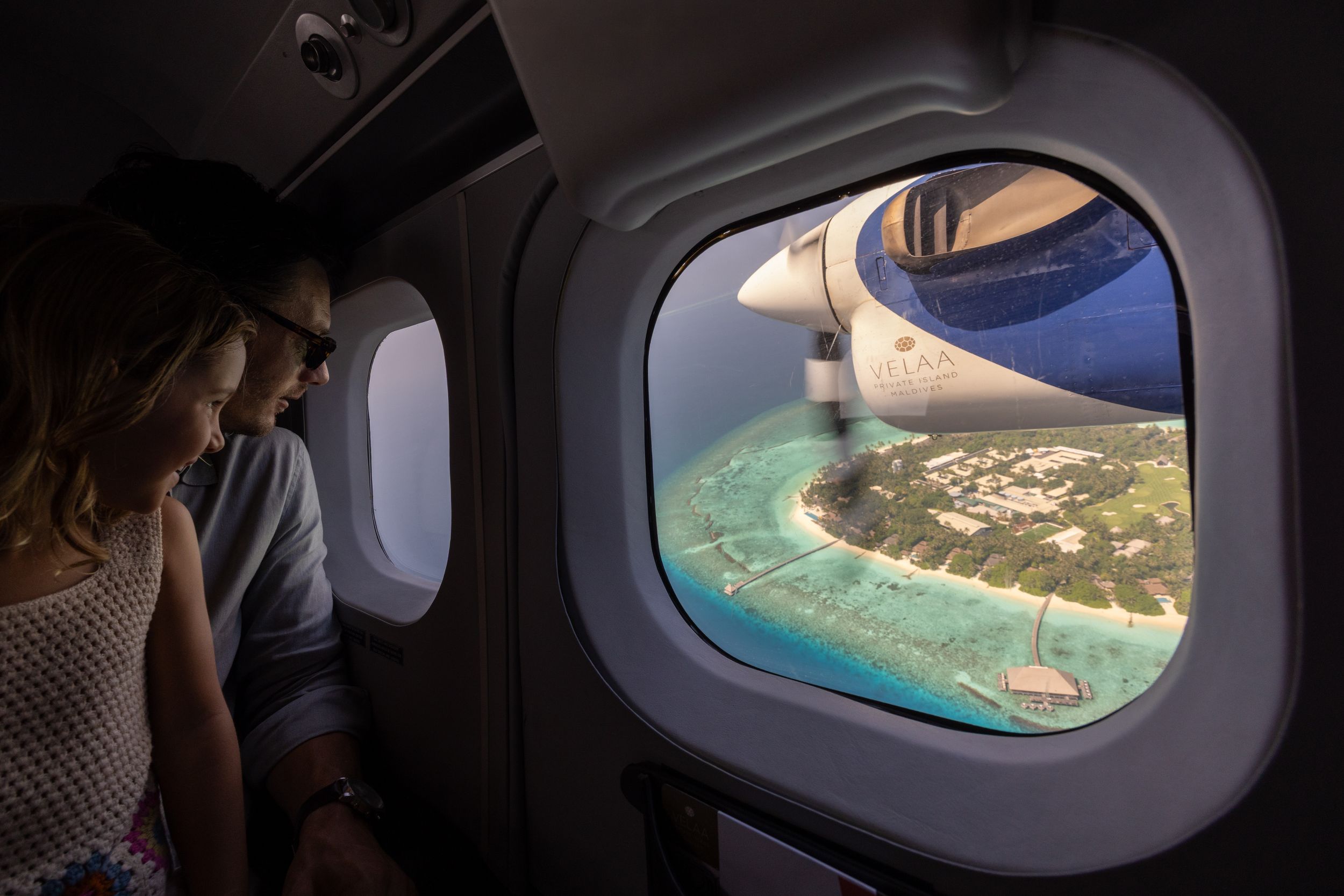 Couple gazing out airplane window at stunning tropical island aerial view below.