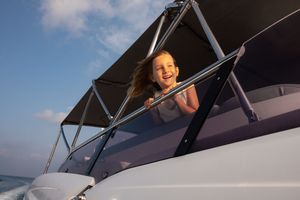 Happy young girl smiling from a luxury yacht deck against a blue sky.