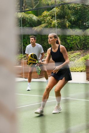 Two players in athletic wear play padel tennis on an outdoor green court surrounded by lush tropical greenery.