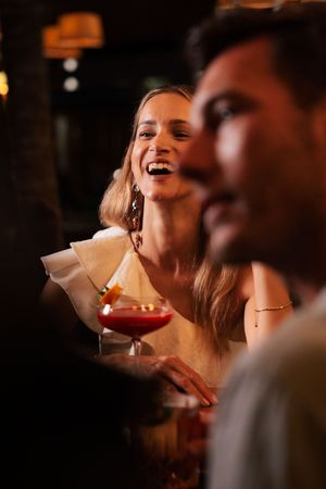Elegant woman laughing at a upscale bar holding a red cocktail at a social gathering.