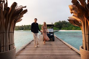 Couple holding hands walking on a wooden pier over turquoise waters at a tropical Maldives resort.