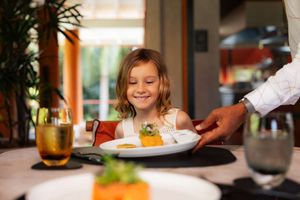 Happy young girl smiling as a waiter serves her a gourmet meal at an elegant restaurant.