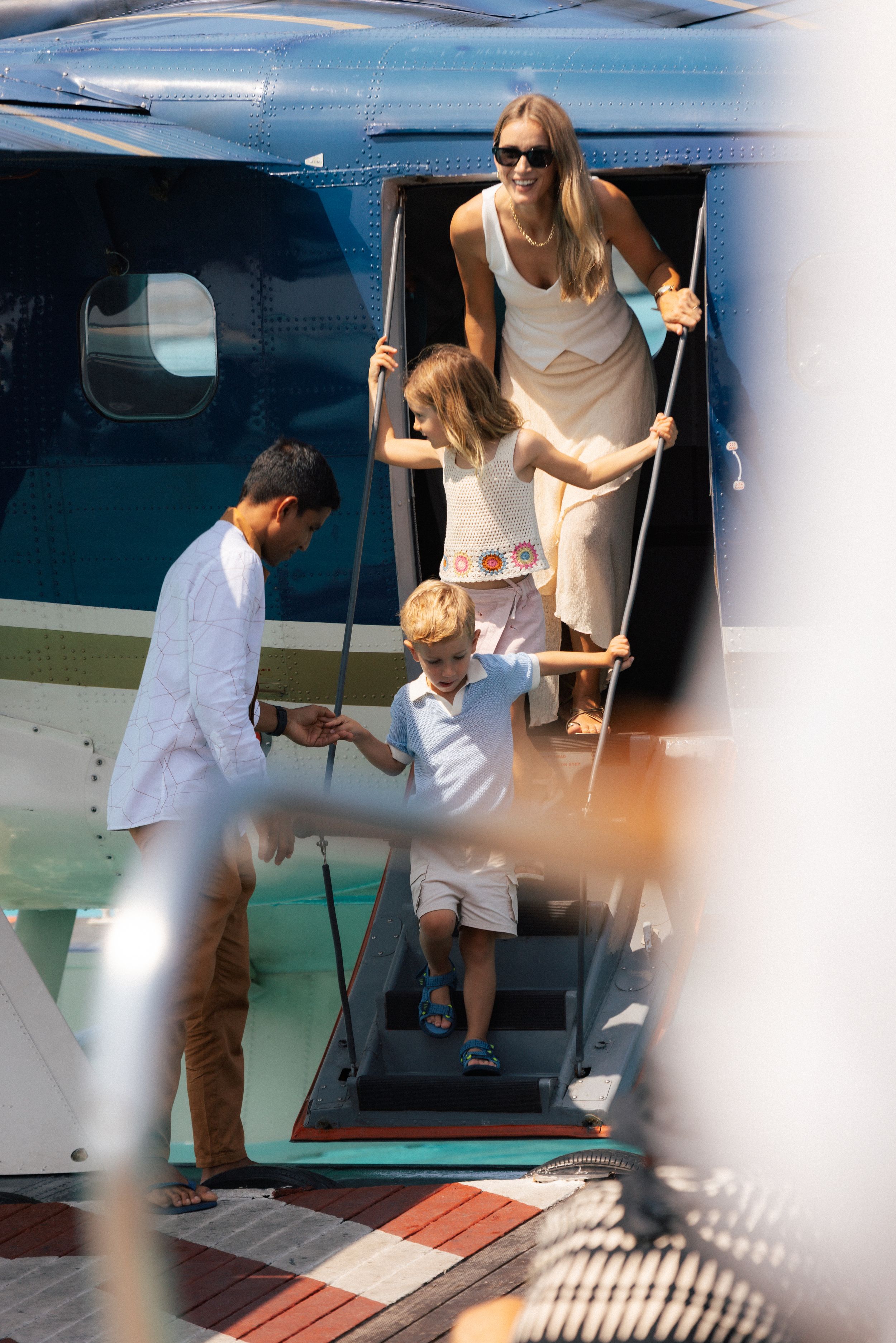 Family disembarking a private helicopter on a sunny day, assisted by a man in white.