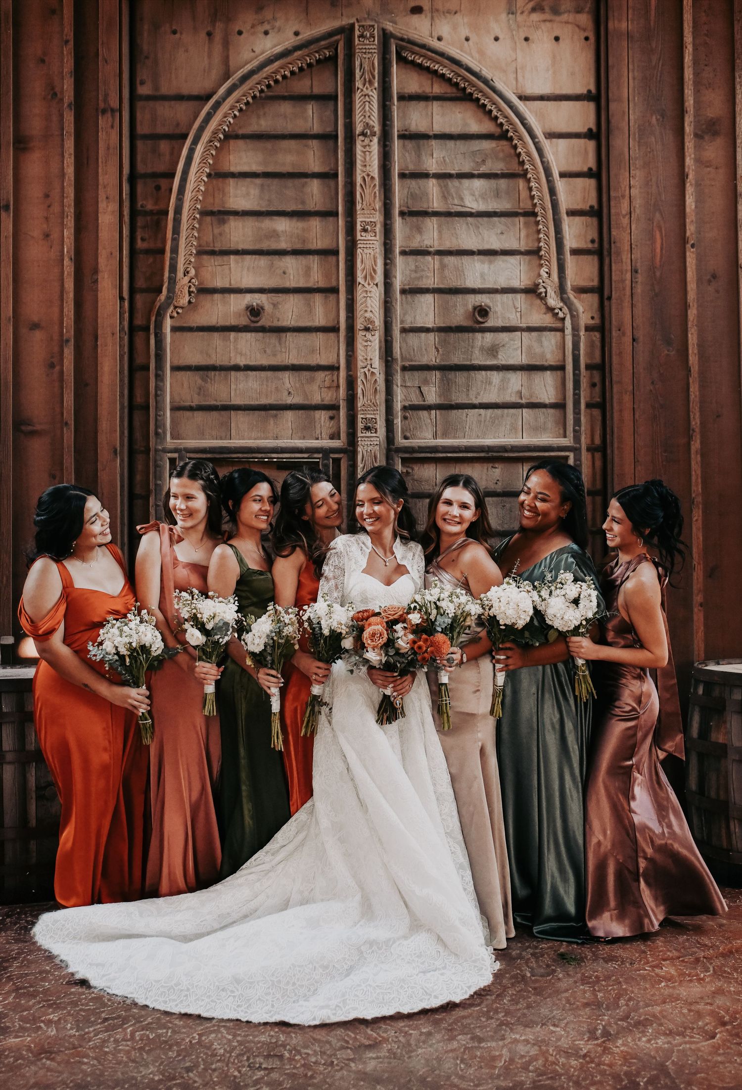 Bridesmaids wearing elegant mismatched fall colored dresses