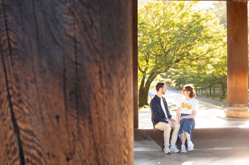 Couple in traditional Japanese attire sitting together under a wooden structure surrounded by lush green trees.