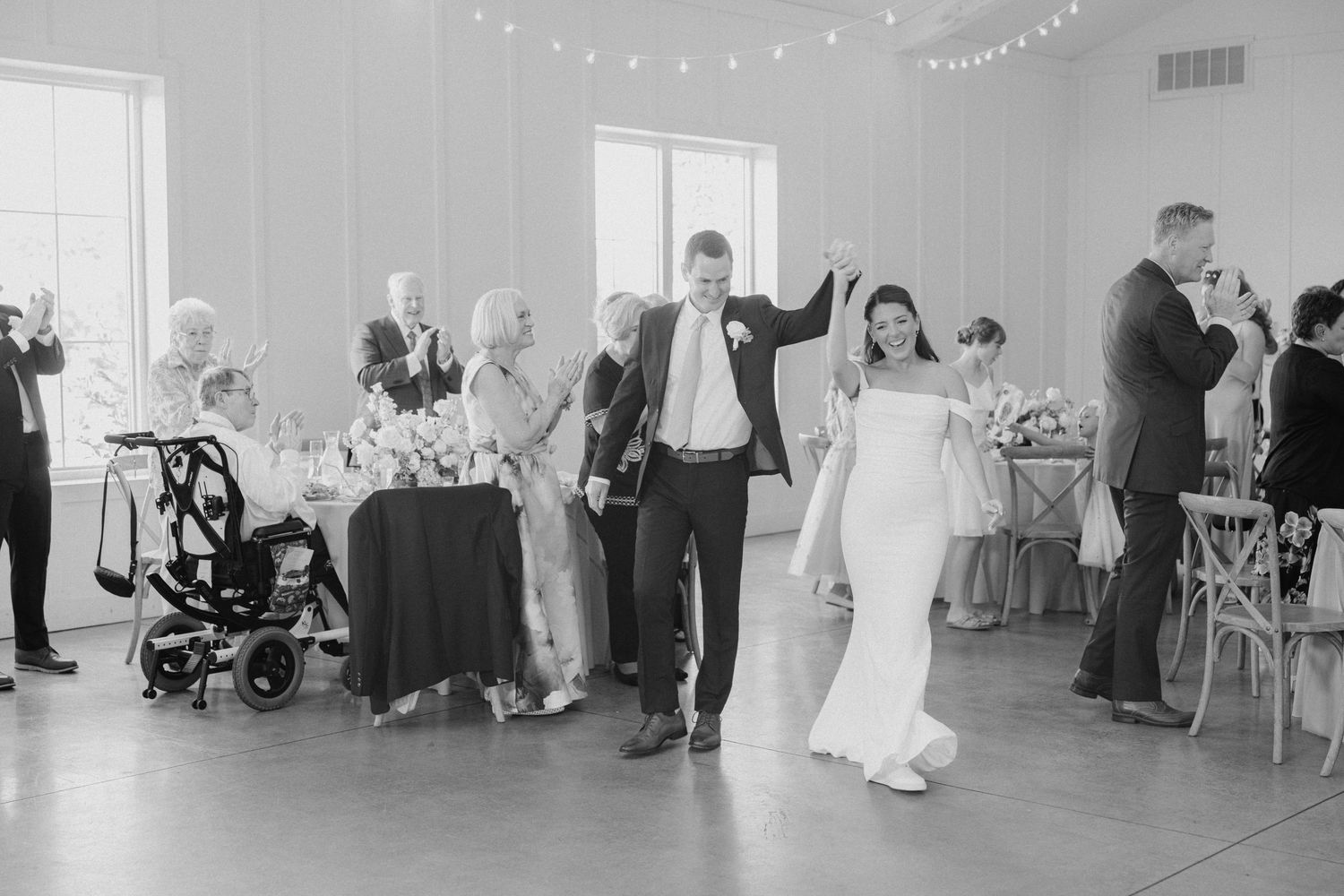 Black and white photo of a couple sharing their first dance at a wedding reception with string lights above.