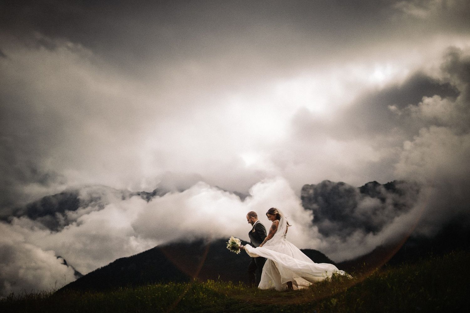Groom dipping his bride for a kiss above a sea of clouds on a mountaintop, by a Canmore wedding photographer