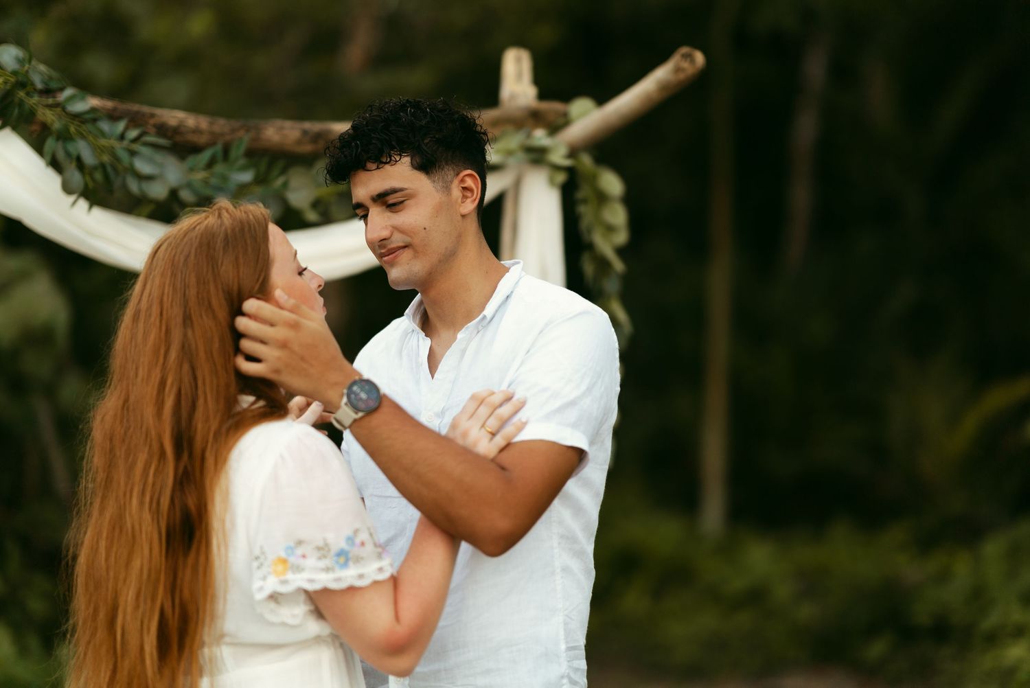 Hispanic man in formal blue button up caressing future redhead wife's face in clothes for beach engagement photos