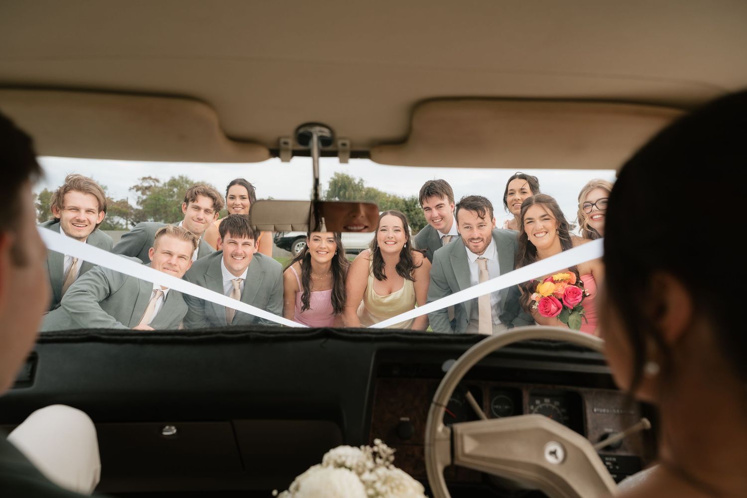 Wedding party waves goodbye to bride and groom through car windshield on their special day.
