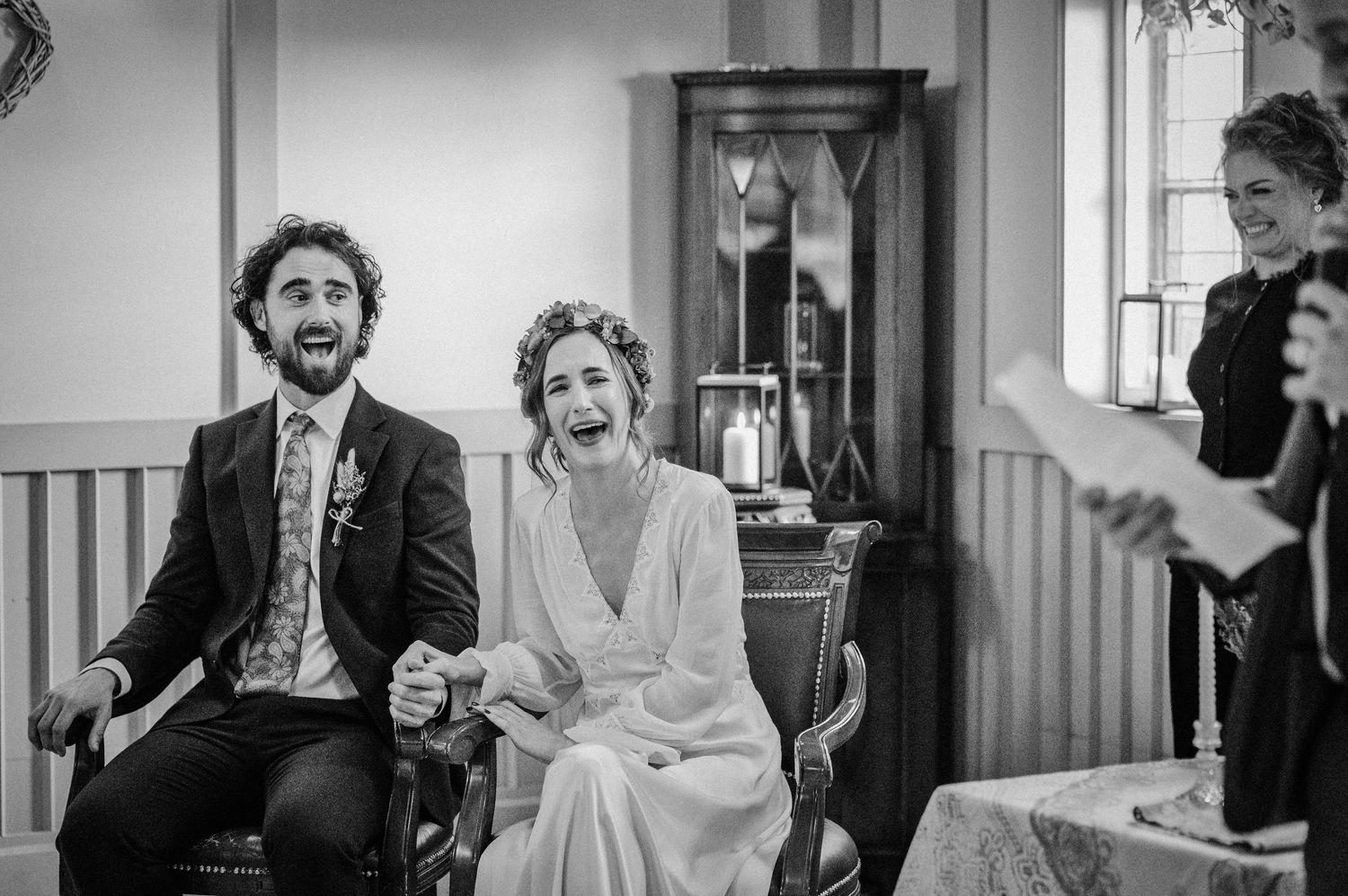 Black and white photo of a joyful bride and groom laughing during their wedding ceremony while seated.