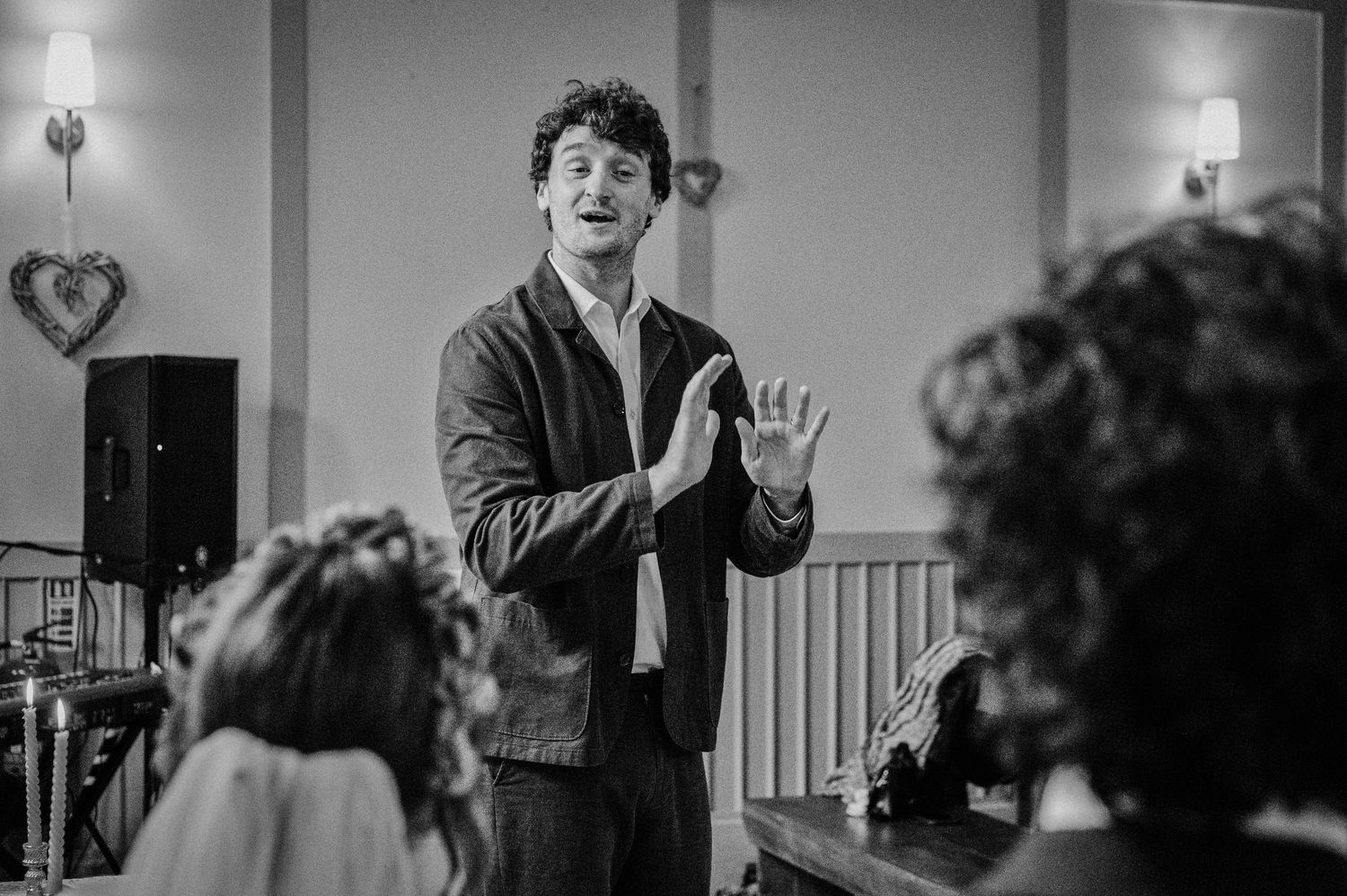 Man speaking animatedly with hand gestures at a wedding reception in black and white photo.