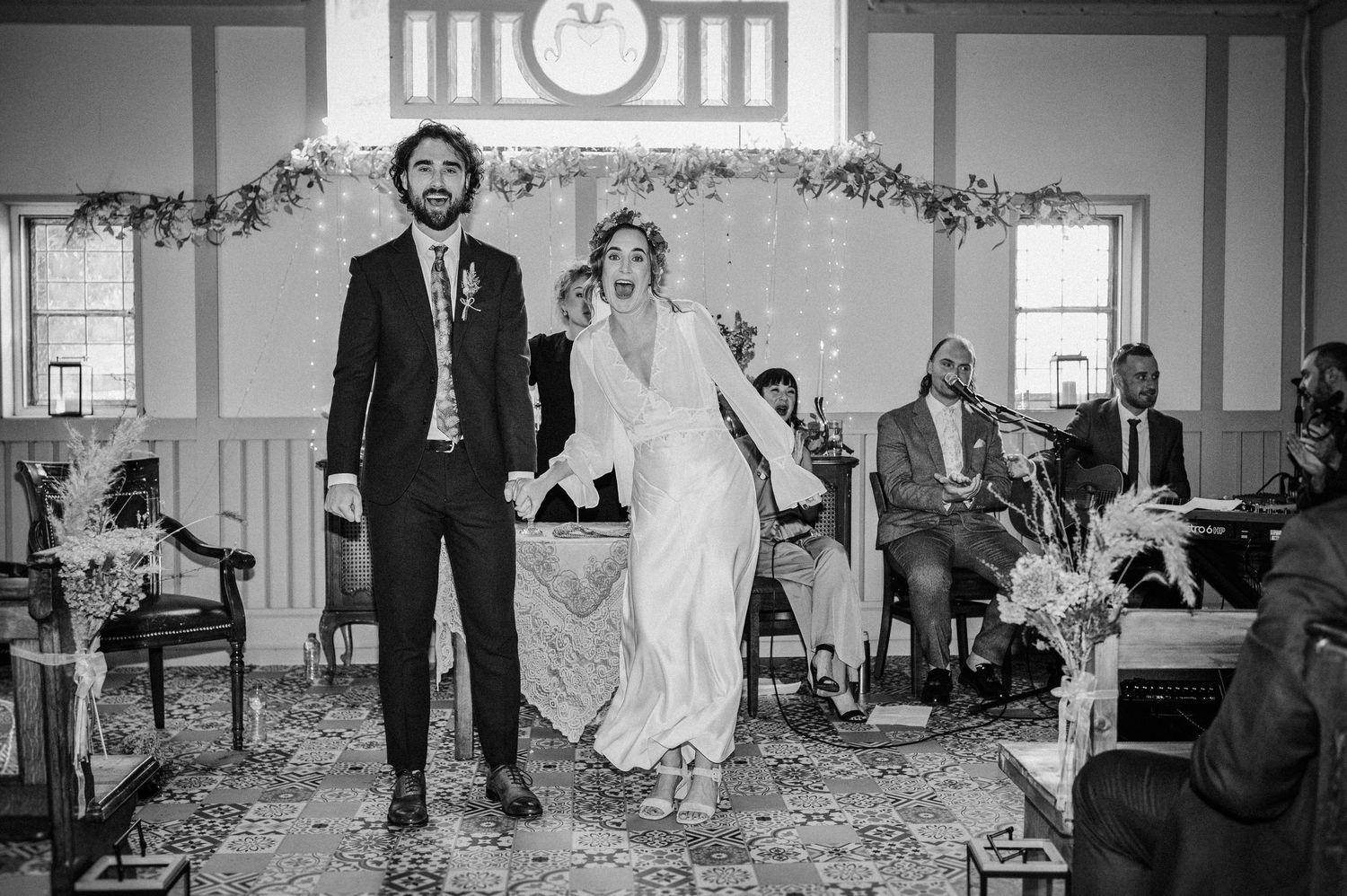 Black and white photo of a newlywed couple walking down the aisle at their indoor wedding ceremony.