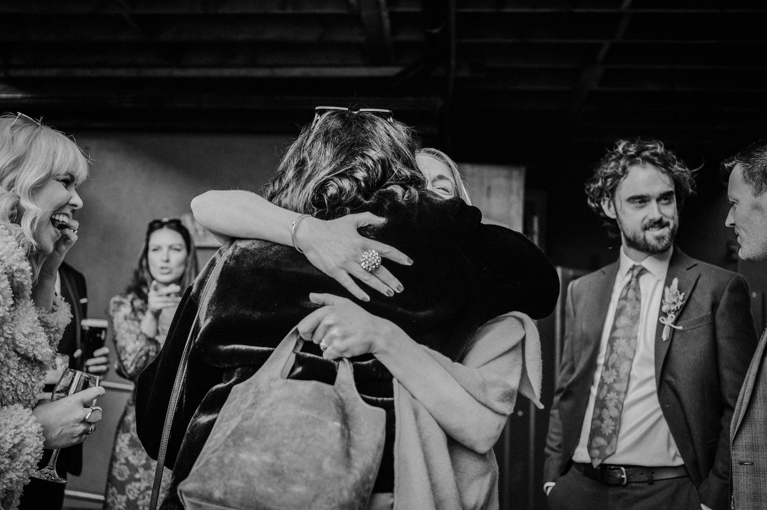 Black and white photo of two guests sharing a warm hug at a wedding reception event.