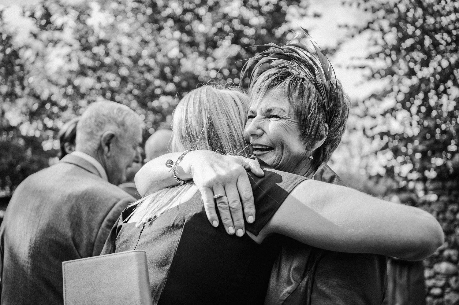 Black and white photo of two women sharing a warm embrace at an outdoor wedding celebration.