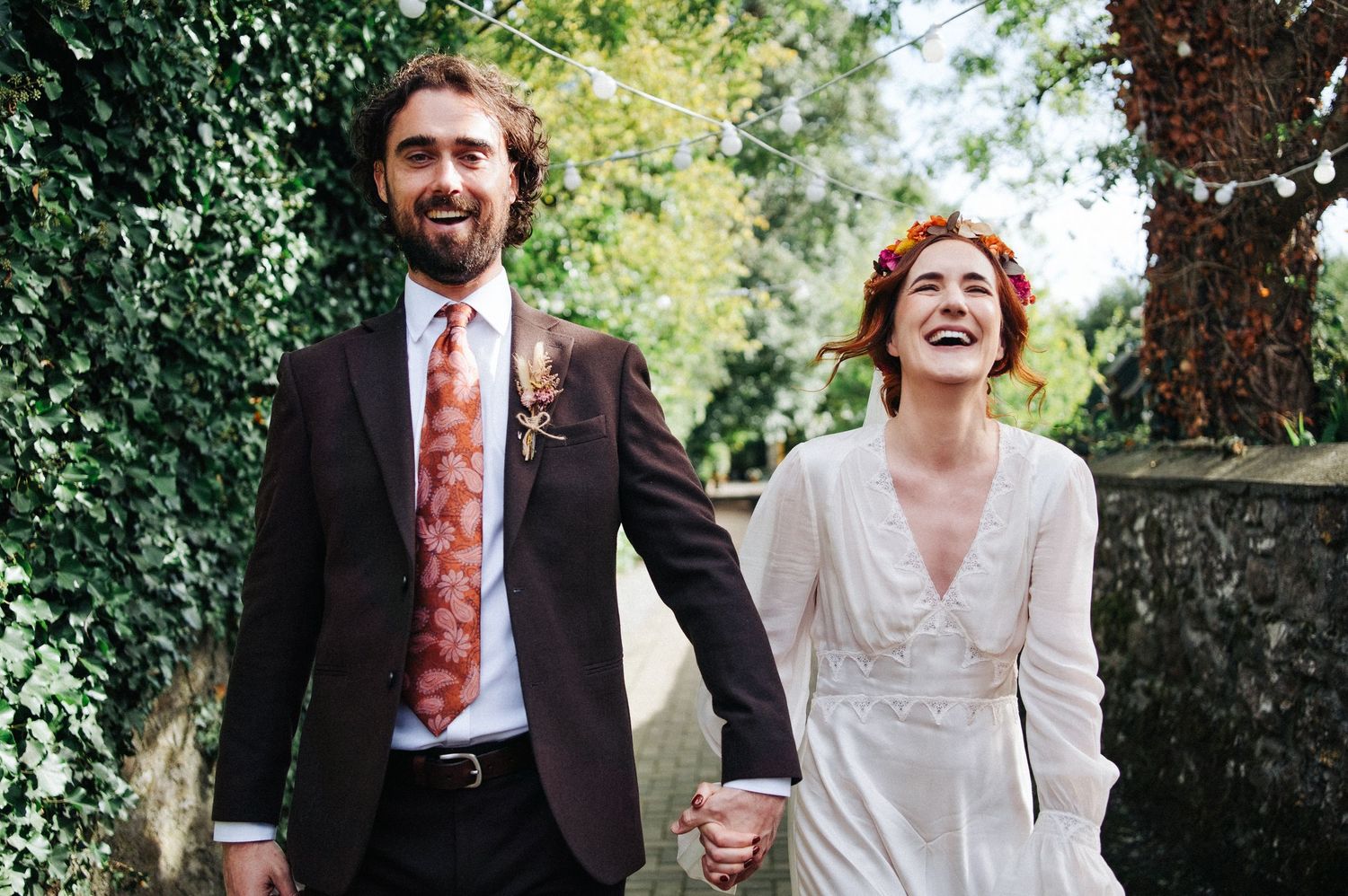 Happy couple holding hands on wedding day, bride in white gown and groom in dark suit with floral tie.