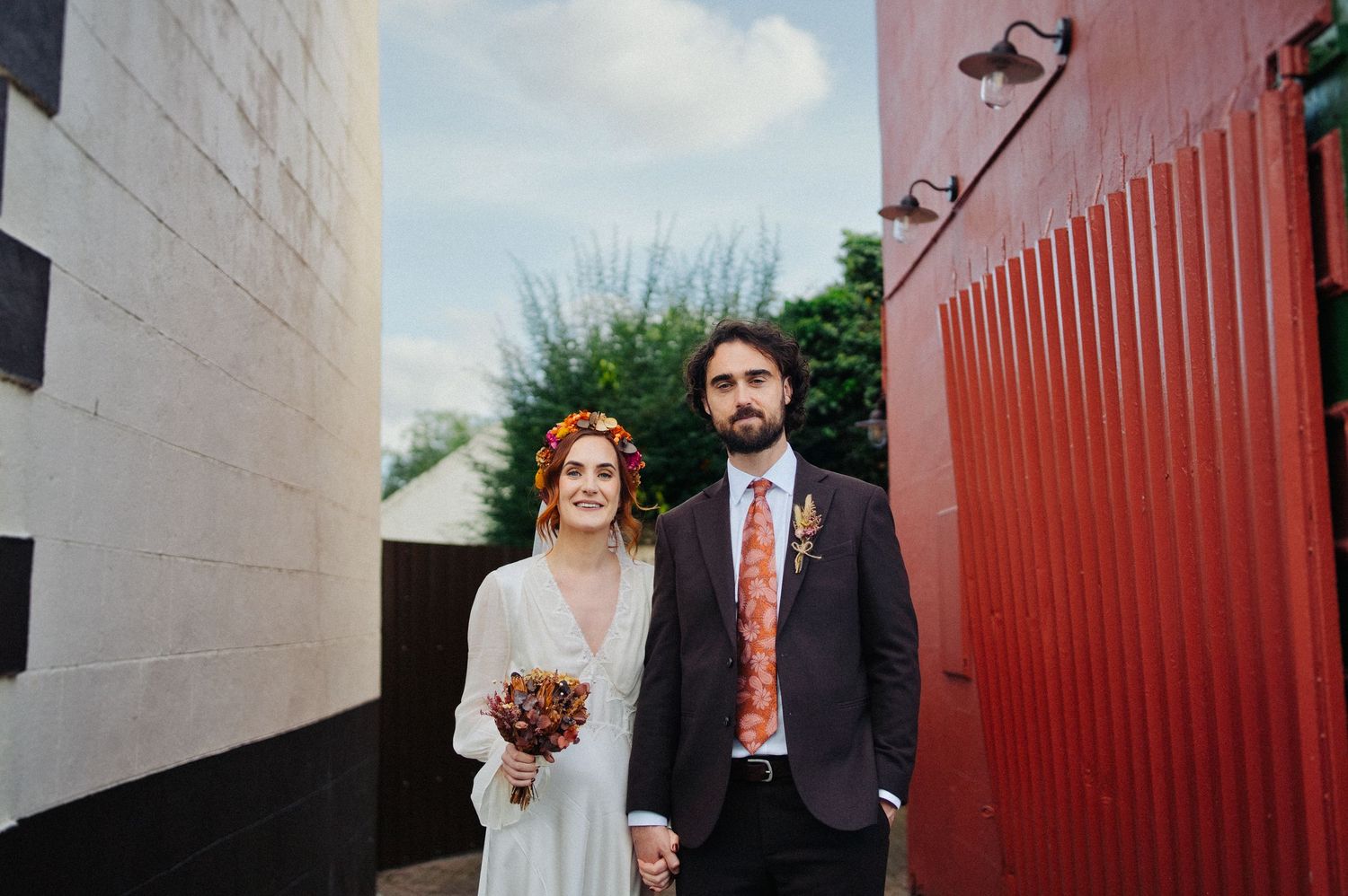 Bride and groom holding hands standing between white and red walls outdoors on their wedding day.