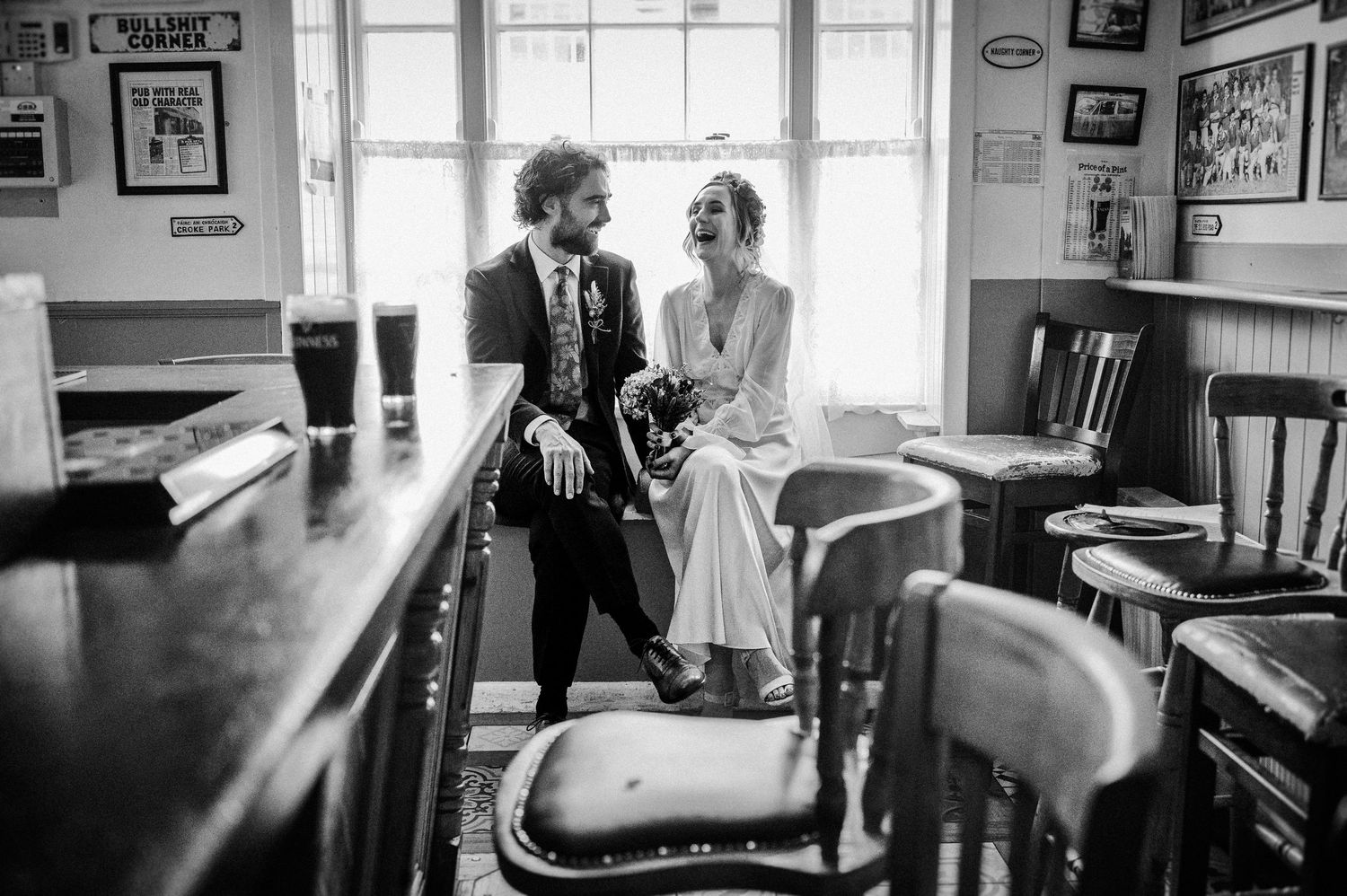 Black and white photo of a bride and groom sharing an intimate moment at a rustic pub bar on their wedding day.