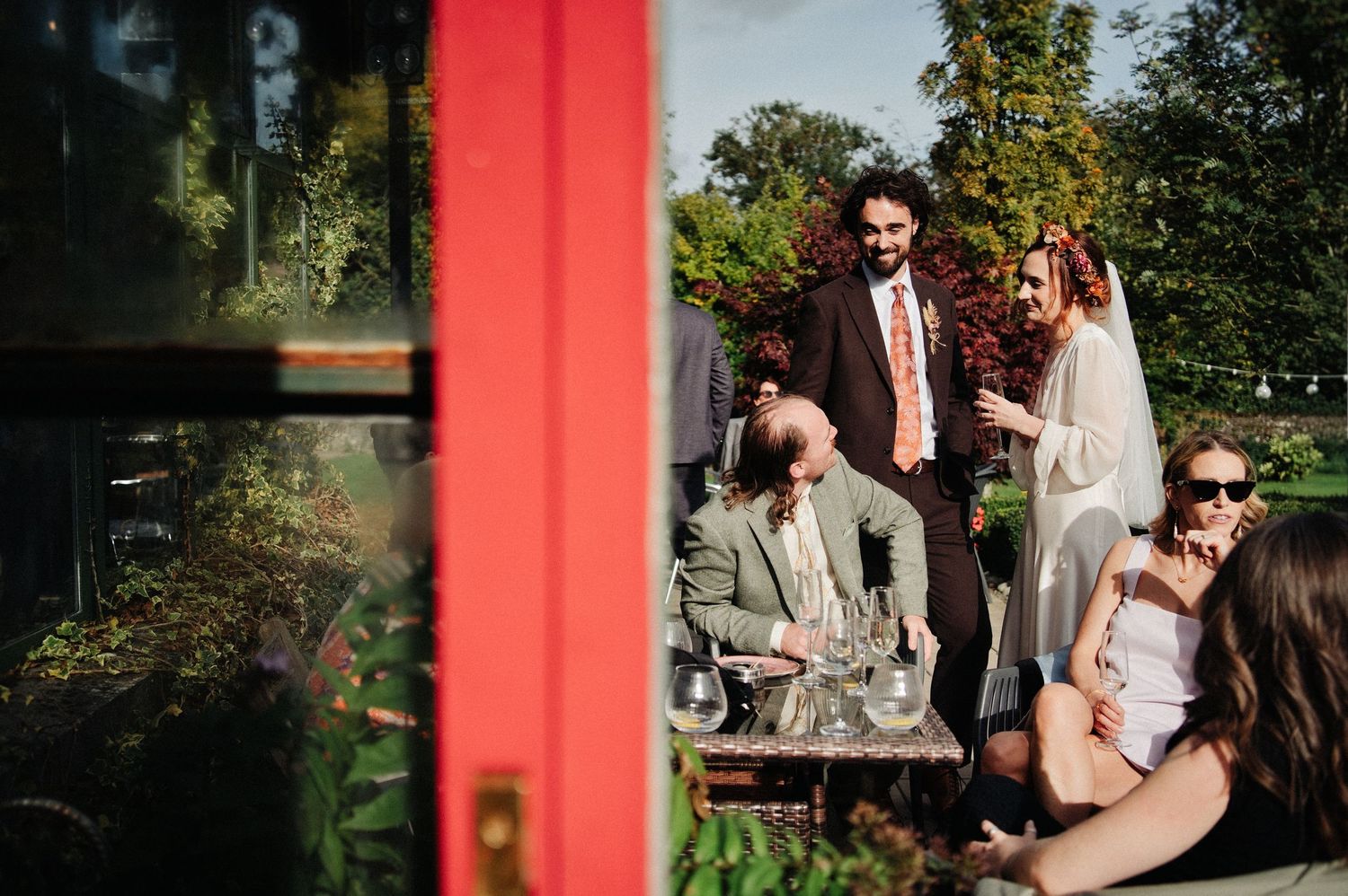 Guests socializing outdoors at a garden party, with a couple standing and others seated near a table with drinks.
