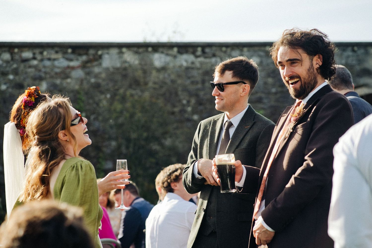 Guests socializing outdoors at a wedding reception, holding champagne glasses and smiling in elegant attire.