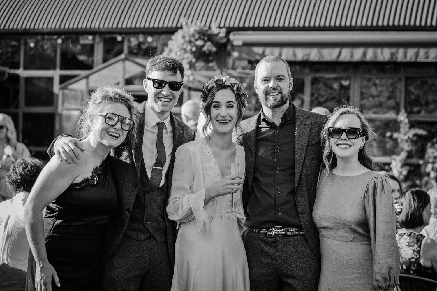 Black and white wedding photo of bride and groom posing with three guests outdoors at a rustic venue.