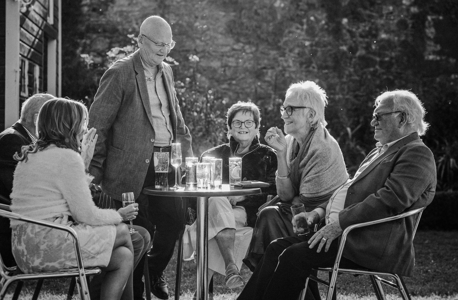 Black and white photo of elderly people socializing at outdoor cafe tables with drinks.