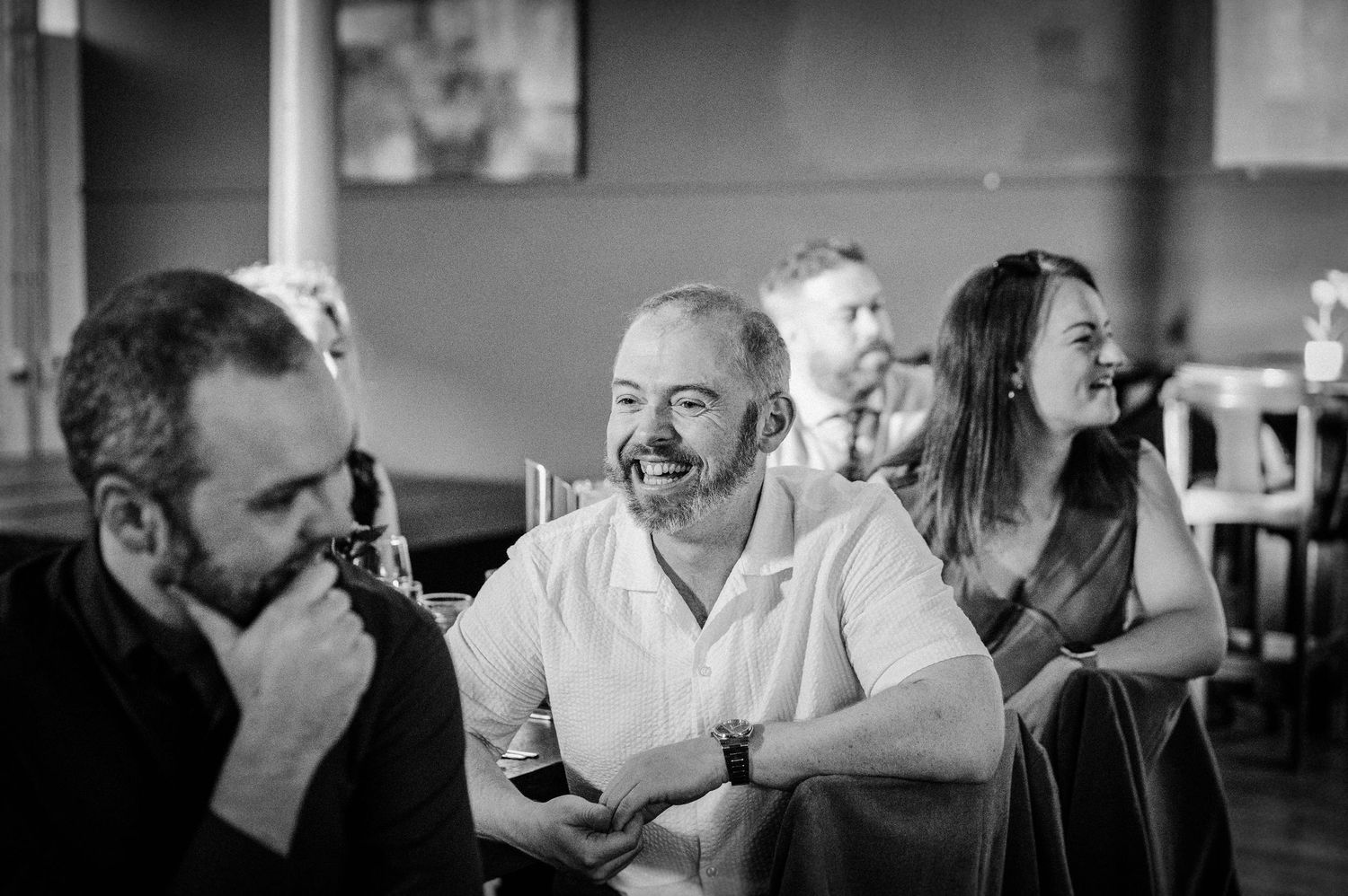 Black and white photo of smiling guests laughing and socializing at an indoor event or gathering.