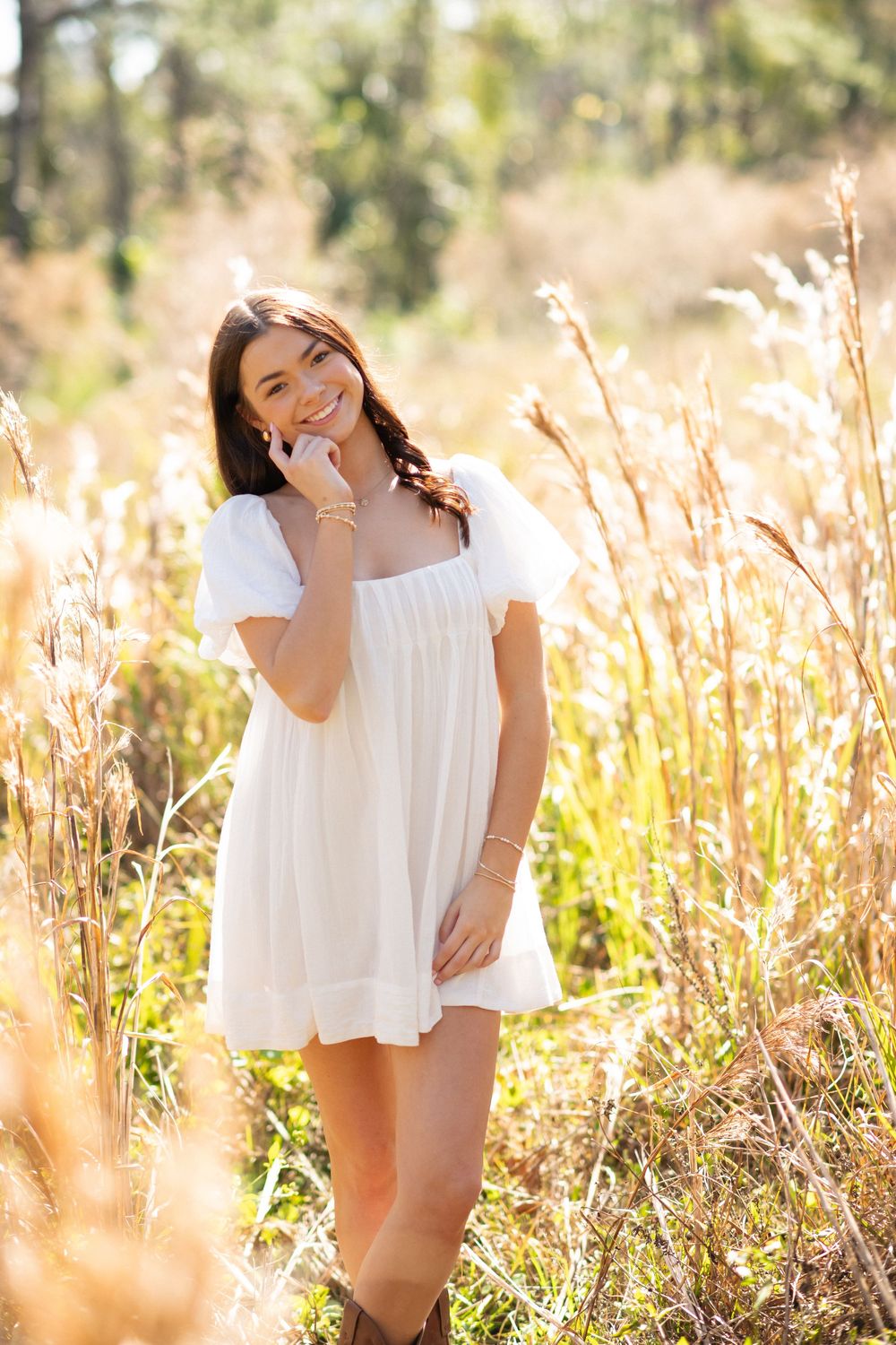 Smiling young woman in white dress standing among tall golden grasses in a sunlit field.