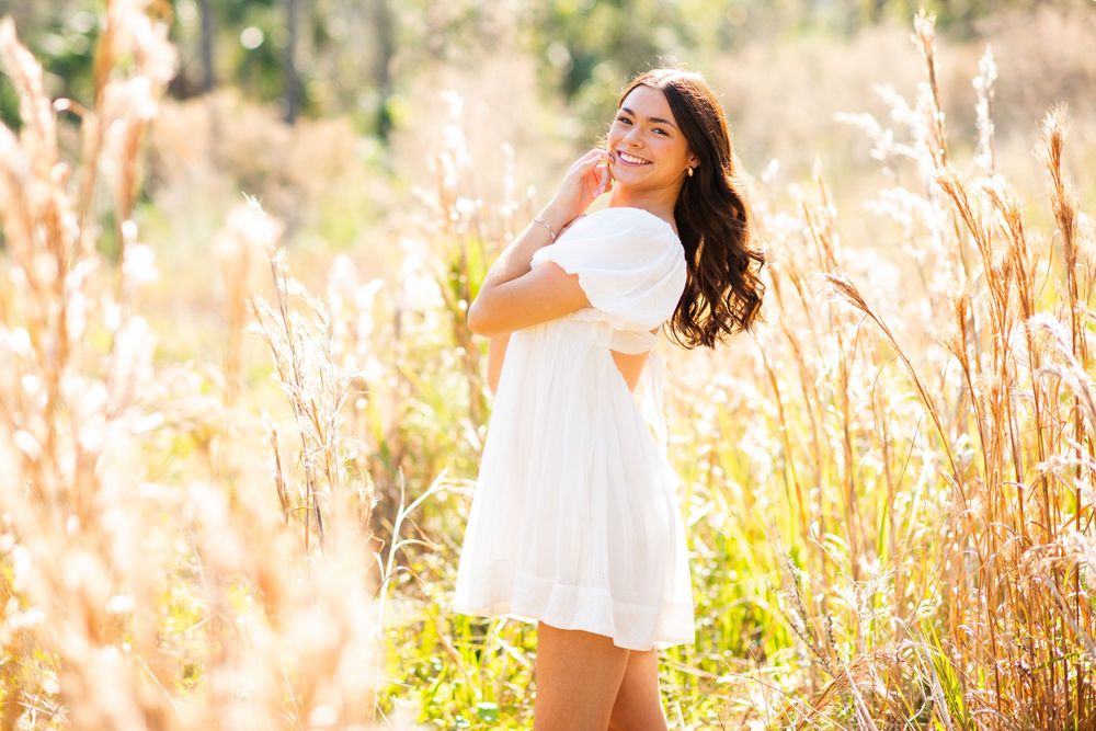 Young woman in white dress smiling among tall golden grasses in a sunlit field.
