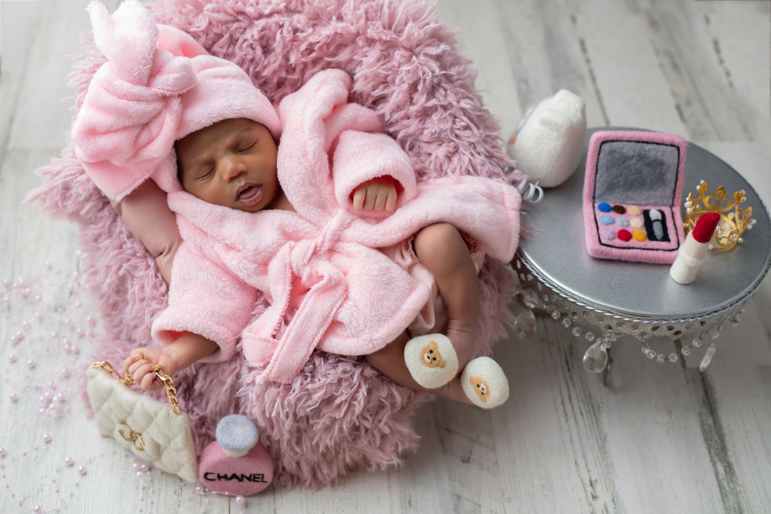 Sleeping newborn in bear outfit nestled between four teddy bears on a white blanket.