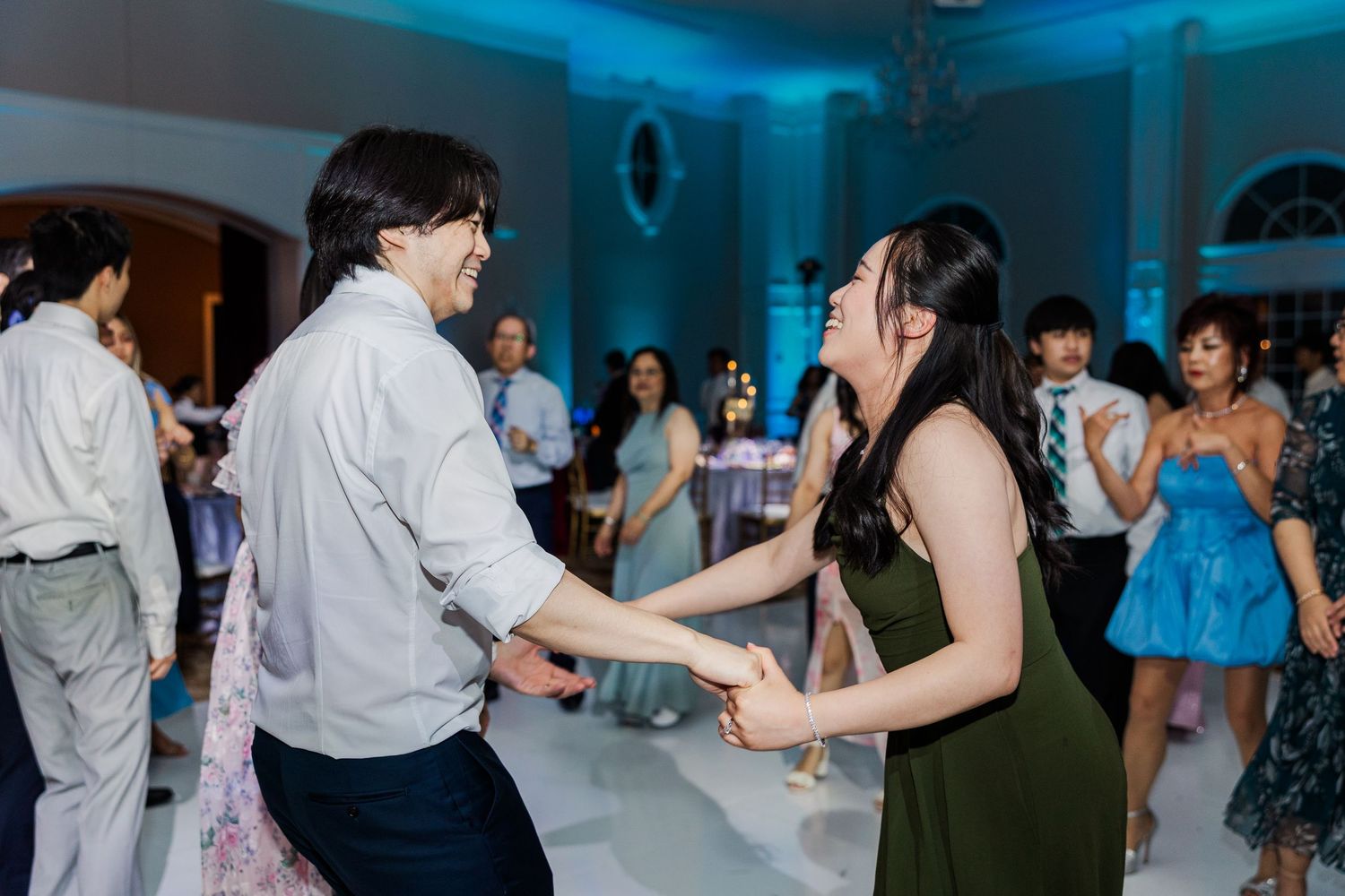 Two guests joyfully dancing together at an elegant wedding reception with blue ambient lighting.
