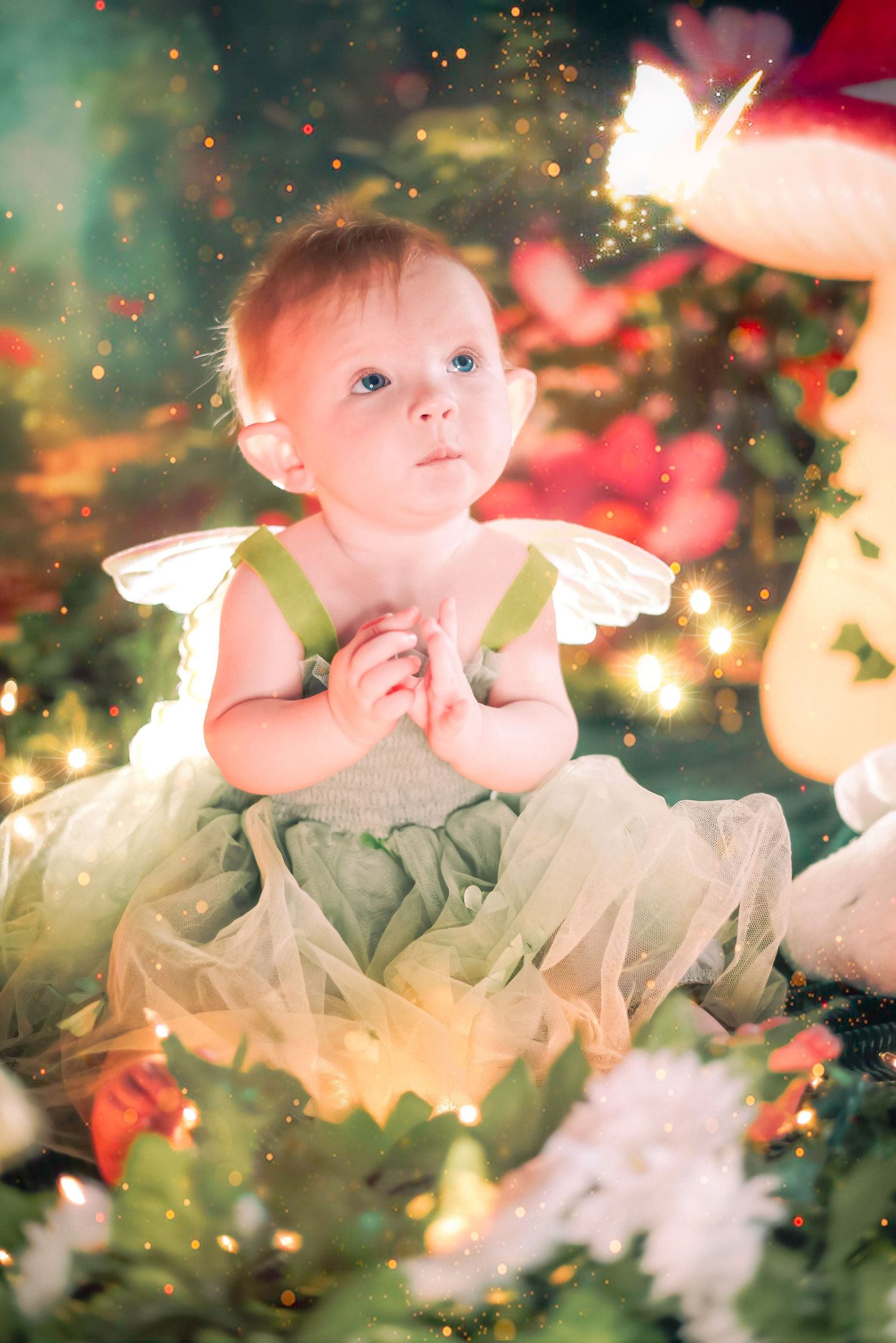 Baby girl in green fairy costume with wings sits among Christmas lights and flowers in enchanted setting at a home session in Lake Worth.