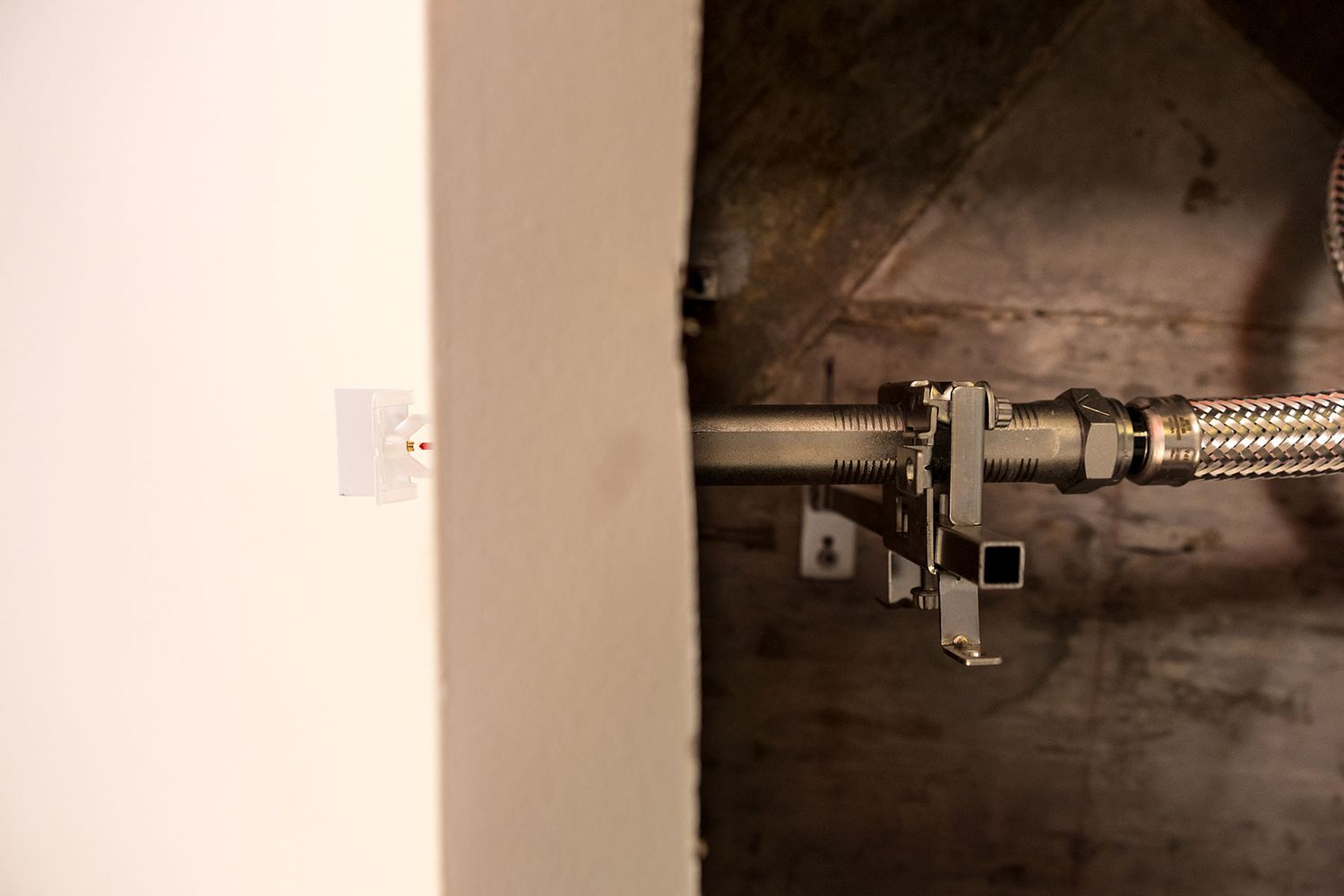 Close-up of a chrome braided flexible water supply line with shut-off valve connected to plumbing in a wall cavity.